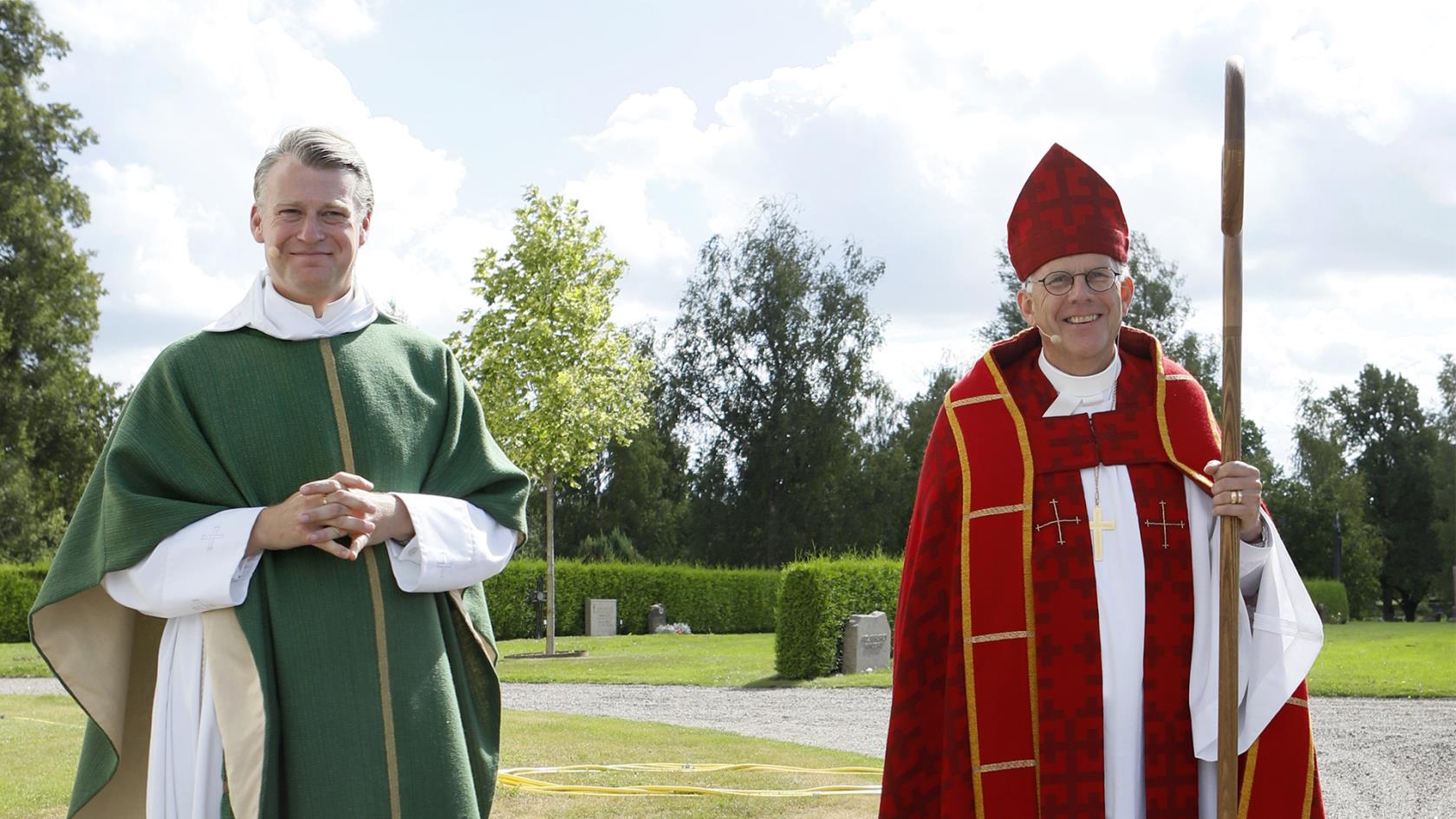 Kyrkoherde Pär Österlund och biskop Martin Modéus står på kyrkogården en fin sommardag, båda klädda i ceremoni-dräkter inför mottagningsmässan.