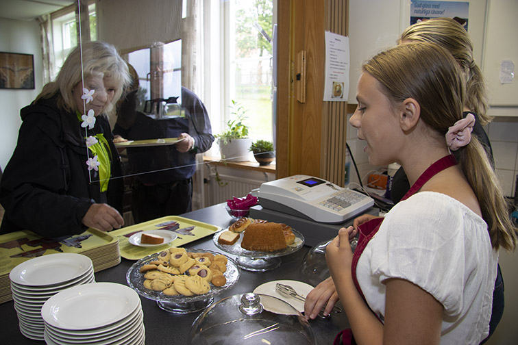 Årets vägkyrka i Habo är lite annorlunda jämfört med tidigare år på grund av coronaviruset. Men öppen är den och det är många glada över. Här ser Selma Andersson och Fiona von Rosen till att Carina Annerkrans får en god fika.