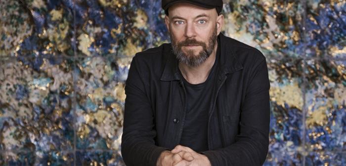 Religionshistorikern David Thurfjell står lutad över ett räcke framför en blåskimrande bergsvägg.