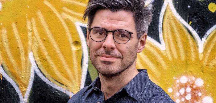 Kyrkohistorikern Joel Halldorf framför en blommig vägg.