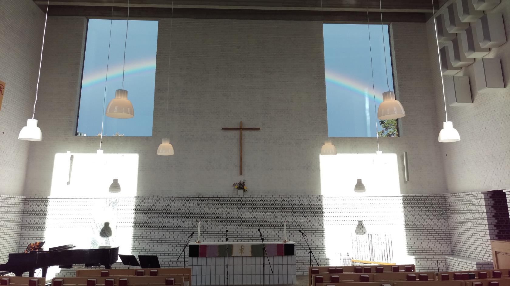 Årsta kyrka interiör med en regnbåge utanför fönstrena