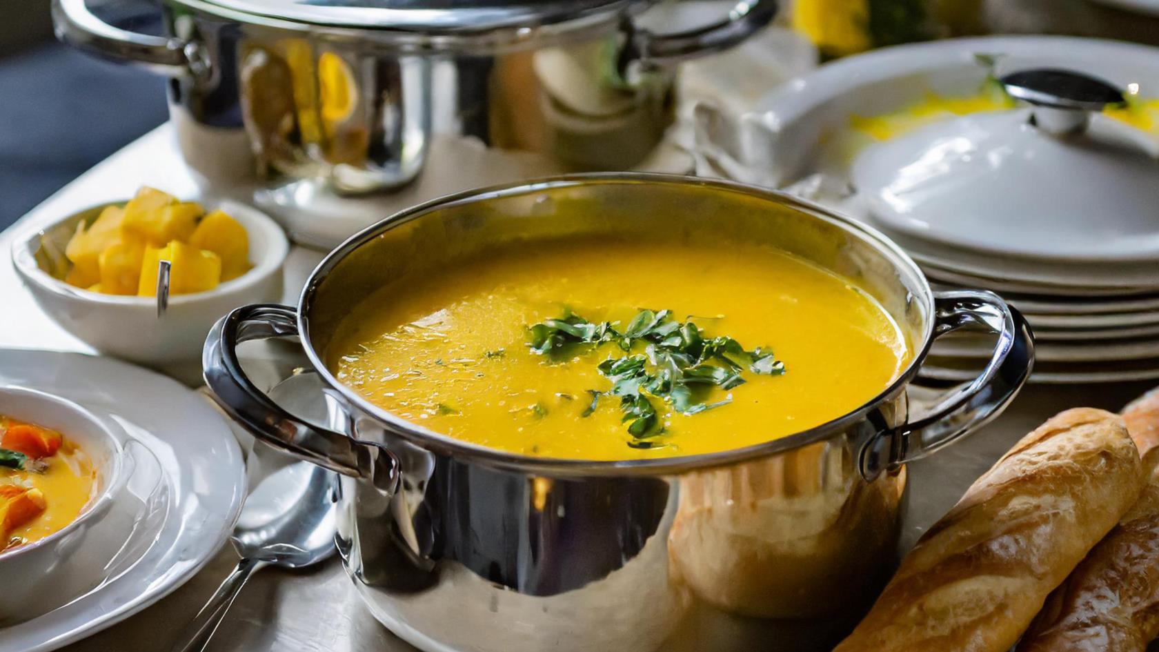 En kastrull med gul soppa på ett dukat bord