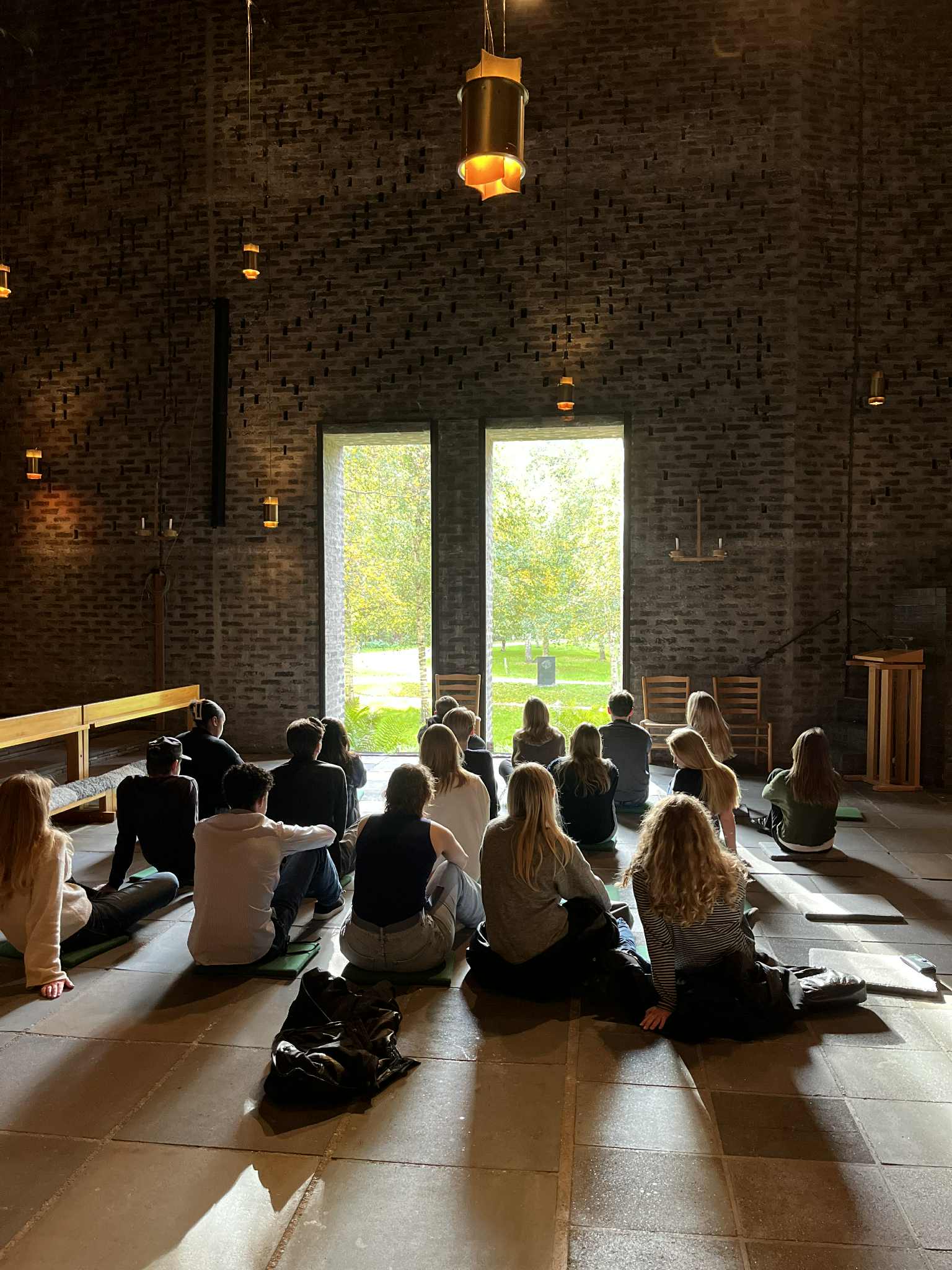 UNgdomar sitter på golvet inne i ett kyrkorum, framför ett stort fönster