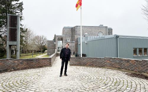 Präst står framför kyrkobyggnad med flagga