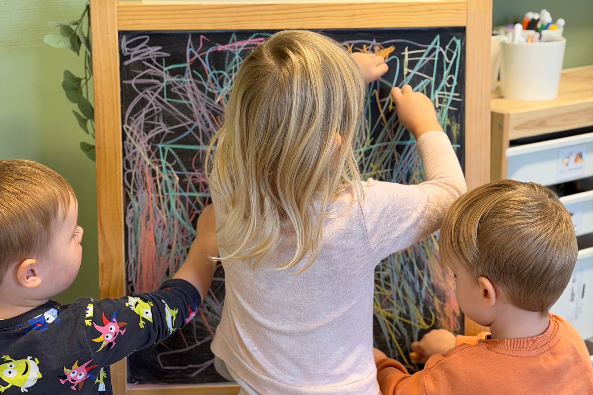 Tre barn ritar på en griffeltavla.