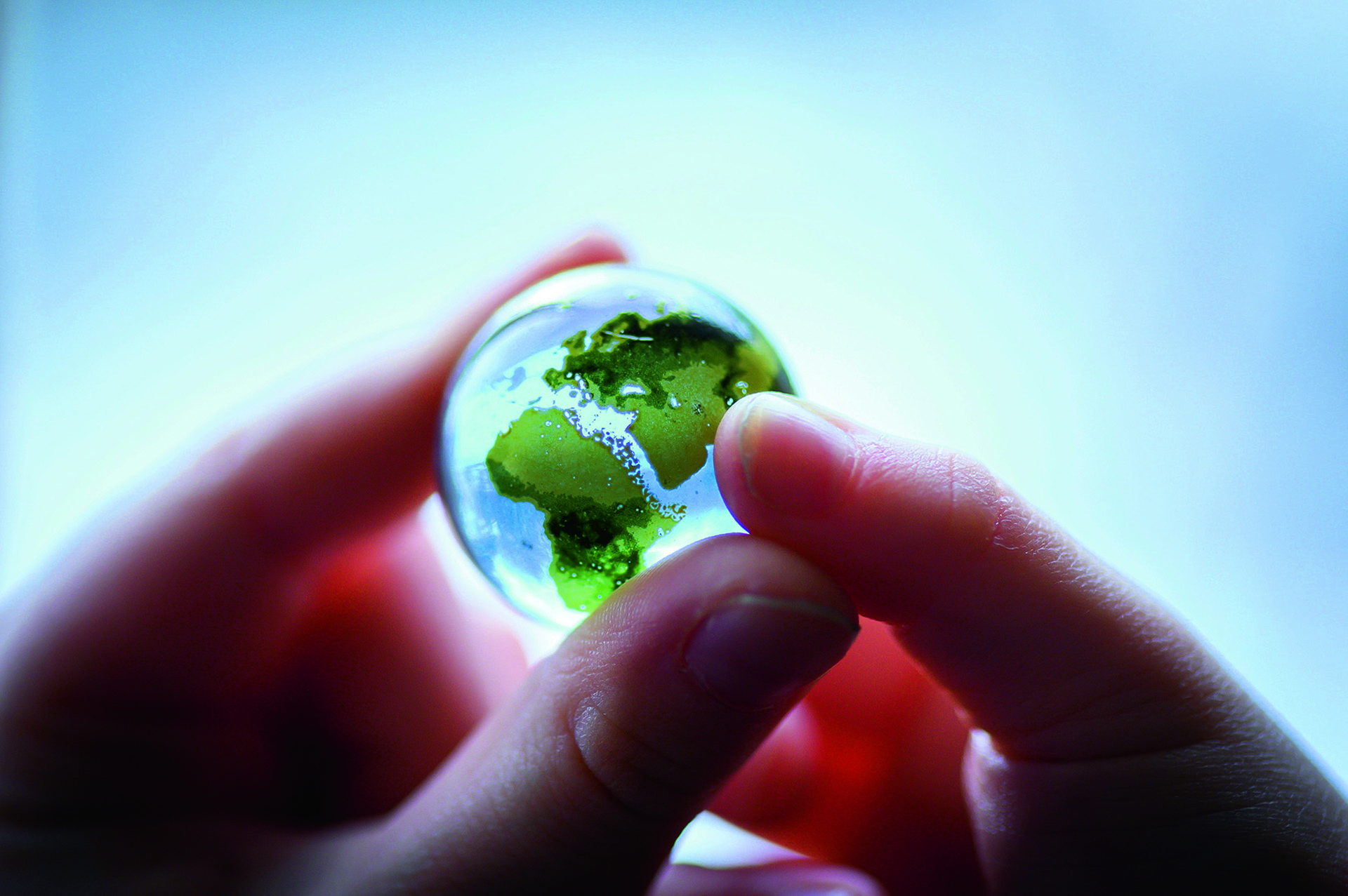 två händer håller i liten jordglob av glas
