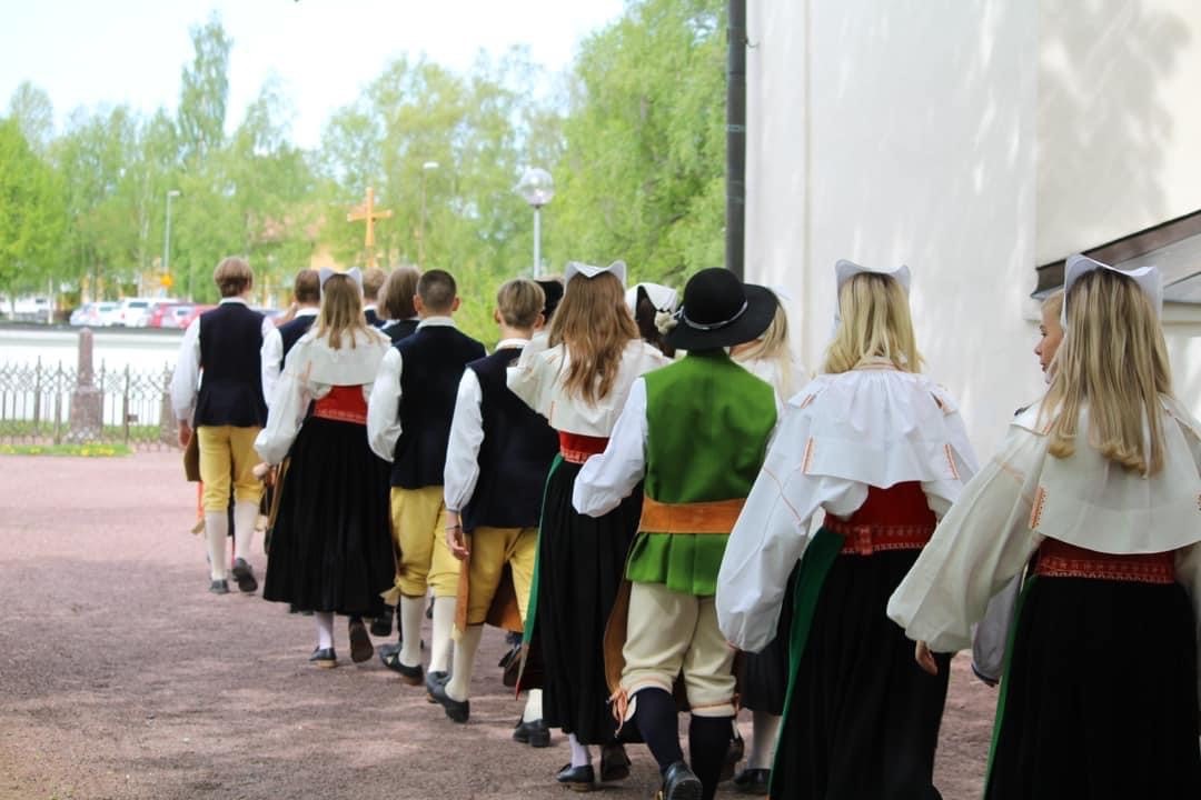 Konfirmander klädda i folkdräkt på väg in i kyrkan.