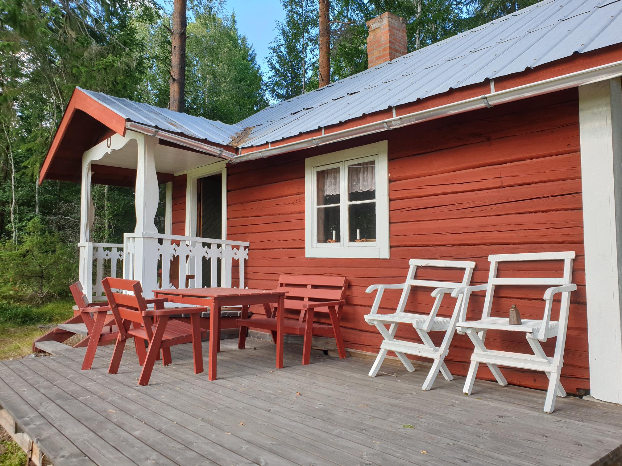 Röd stuga med några vita och röda stolar utanför på altanen