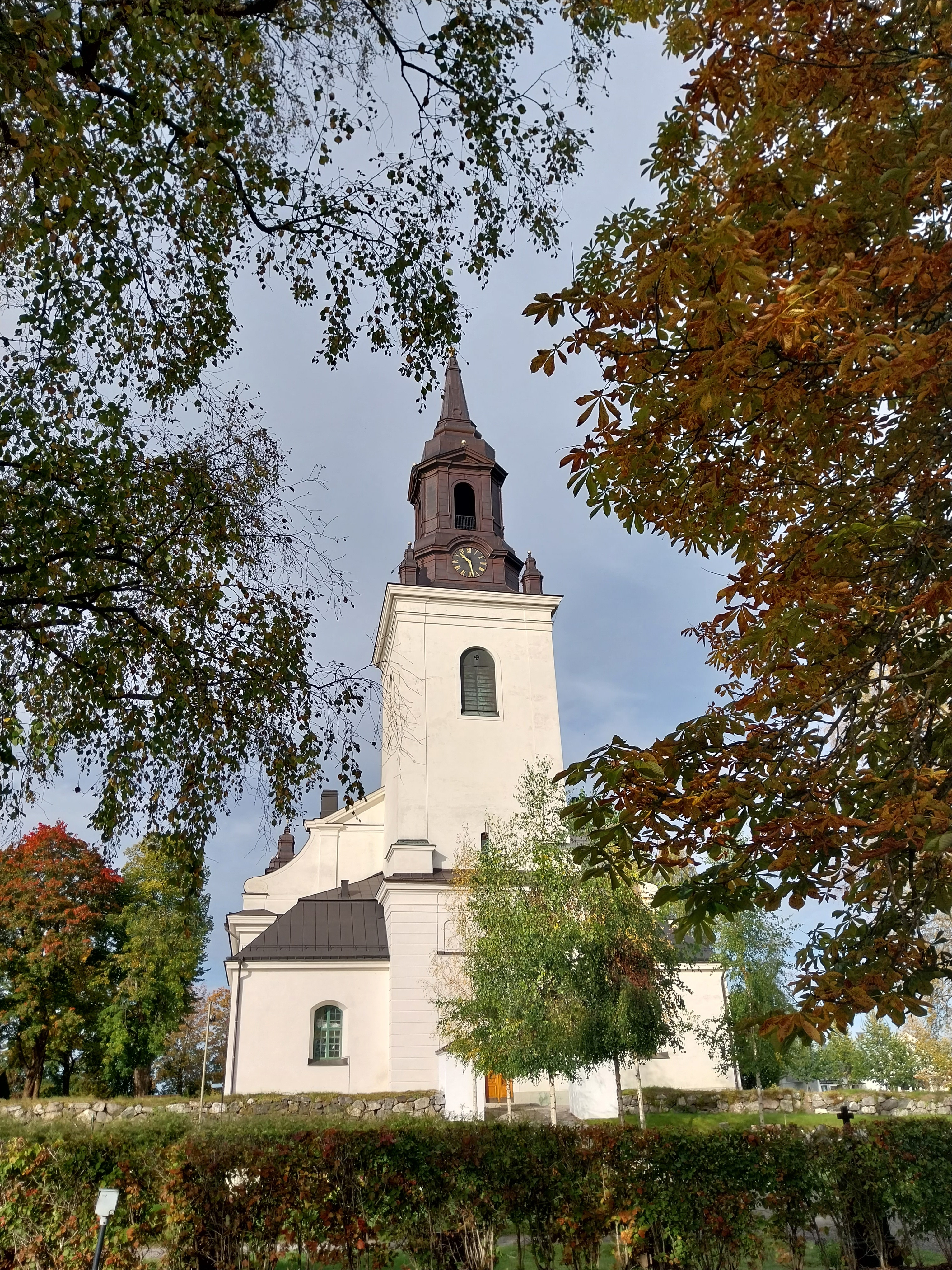 Vit kyrka med svart tak och några träd som grönskar