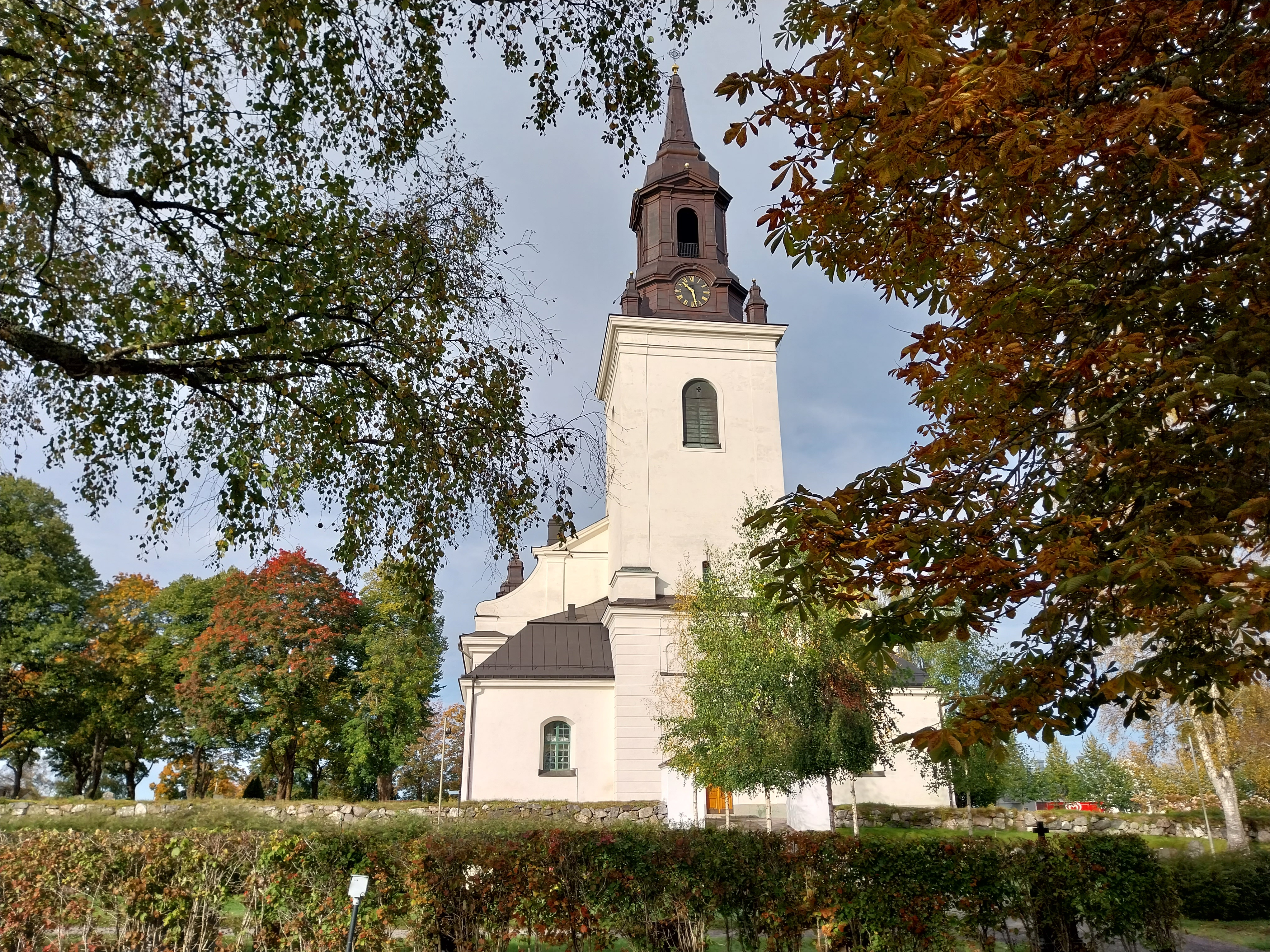 Vit kyrka med svart tak och några träd som grönskar