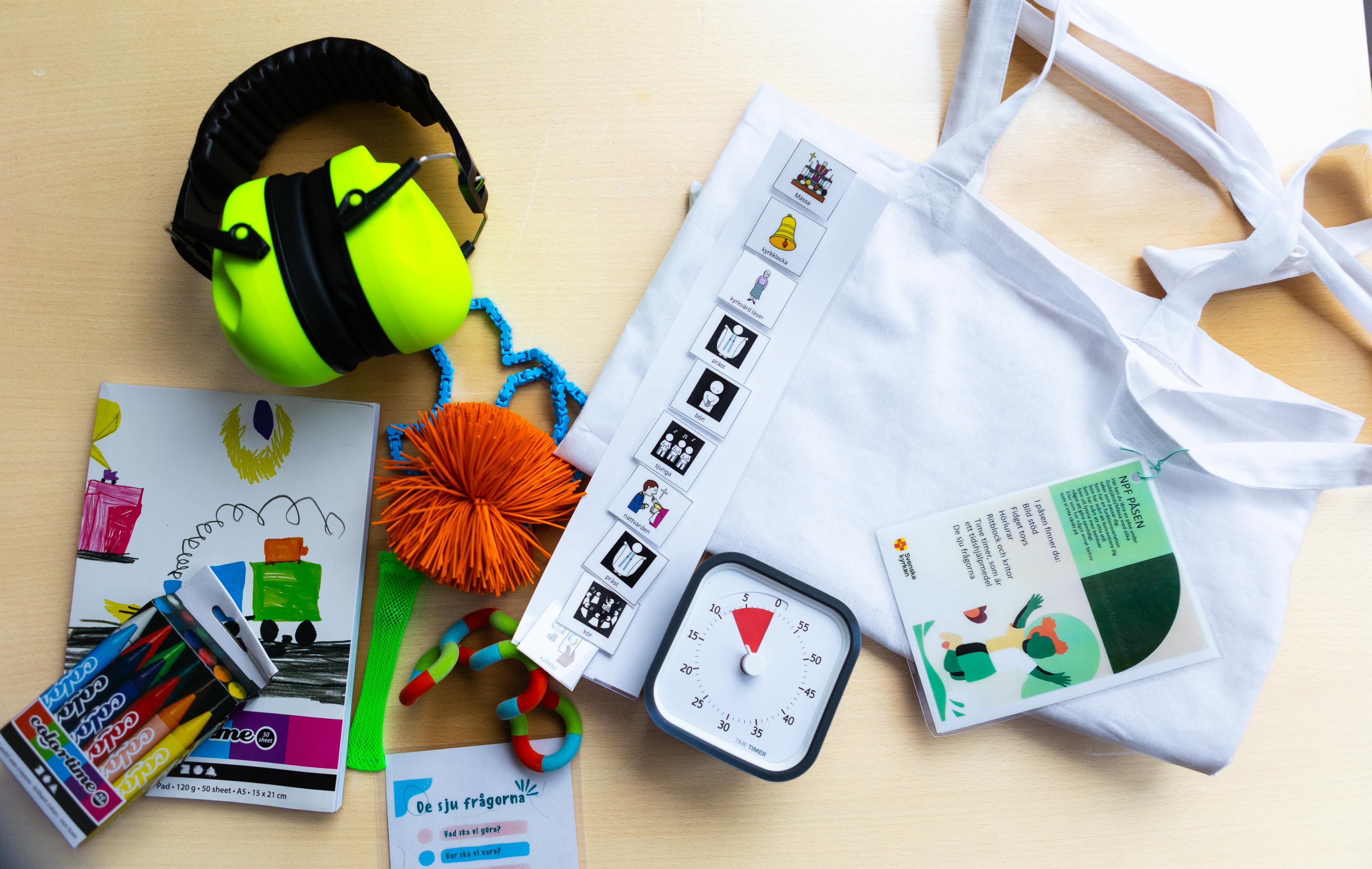 En påse med olika hjälpmedel bredvid, hörselkåpor, time timer, ritblock, fidget-toys