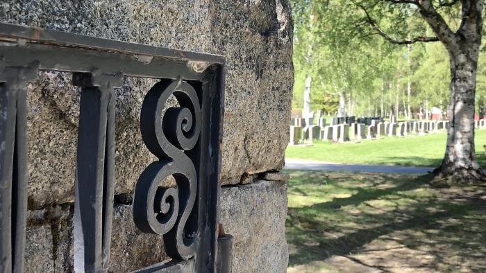 Sten mur med en järngrind som leder in till en grönskande kyrkogård.