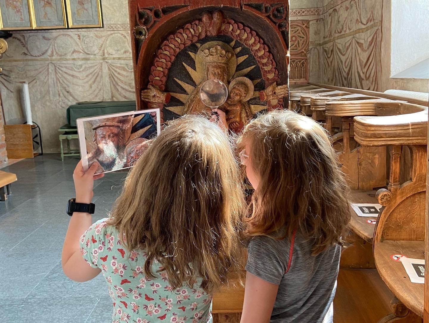 Två flickor går på upptäcktsfärd i kyrkan med bilder som ledtrådar.