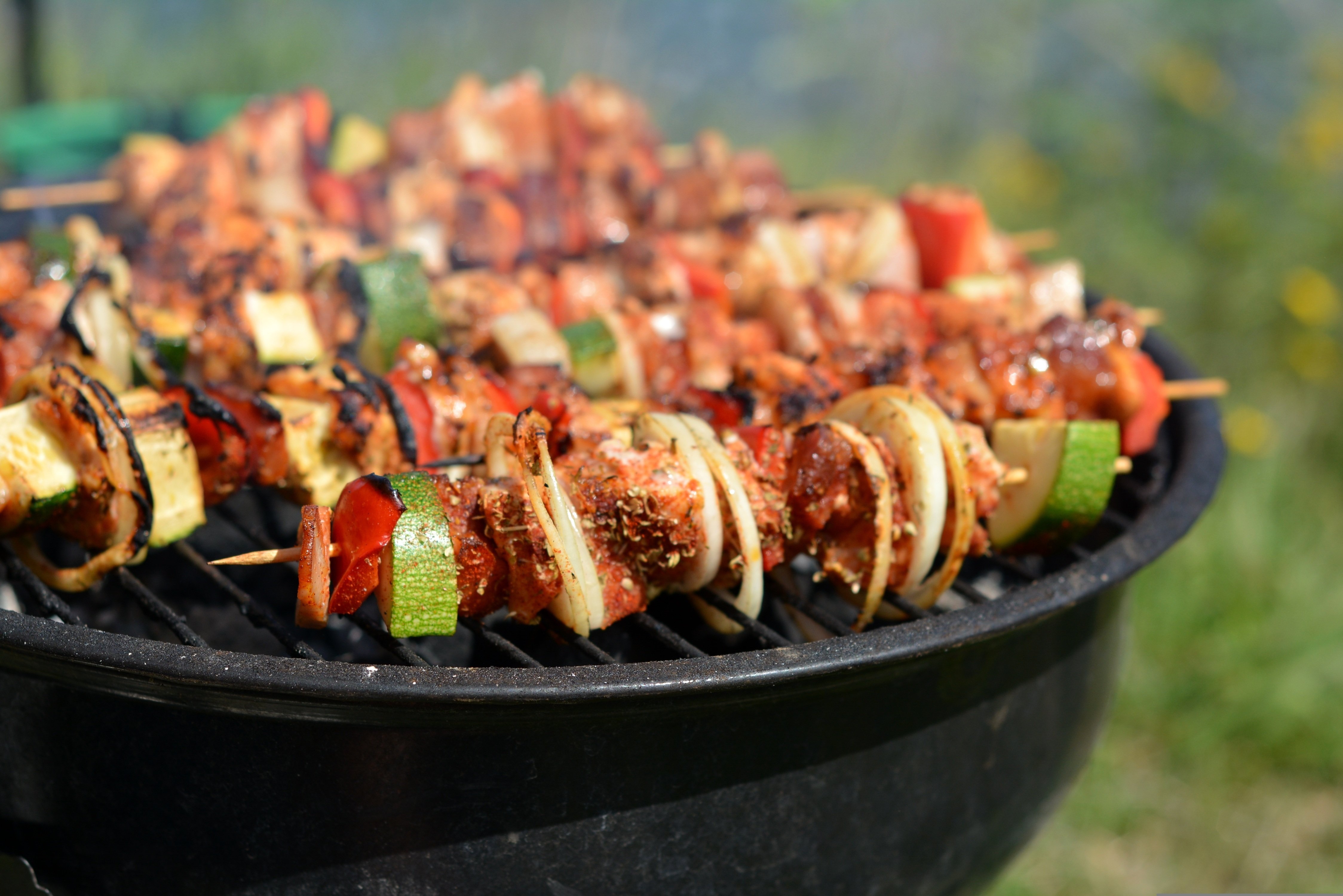 På bilden syns grillspett påen utegrill. På grillspetten finns kycklingbitar, paprika, squash och lök.