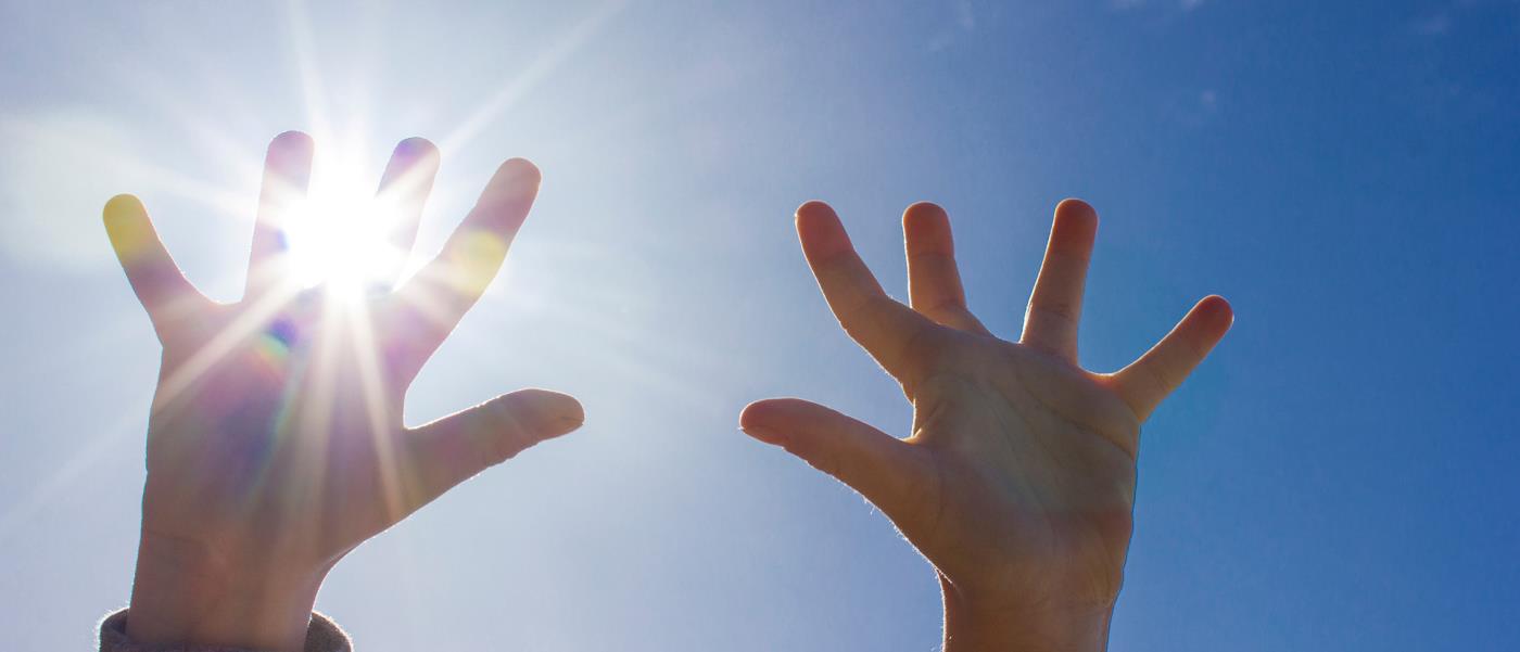 Barnhänder sträckta mot himlen med solstrålar mellan fingrarna.