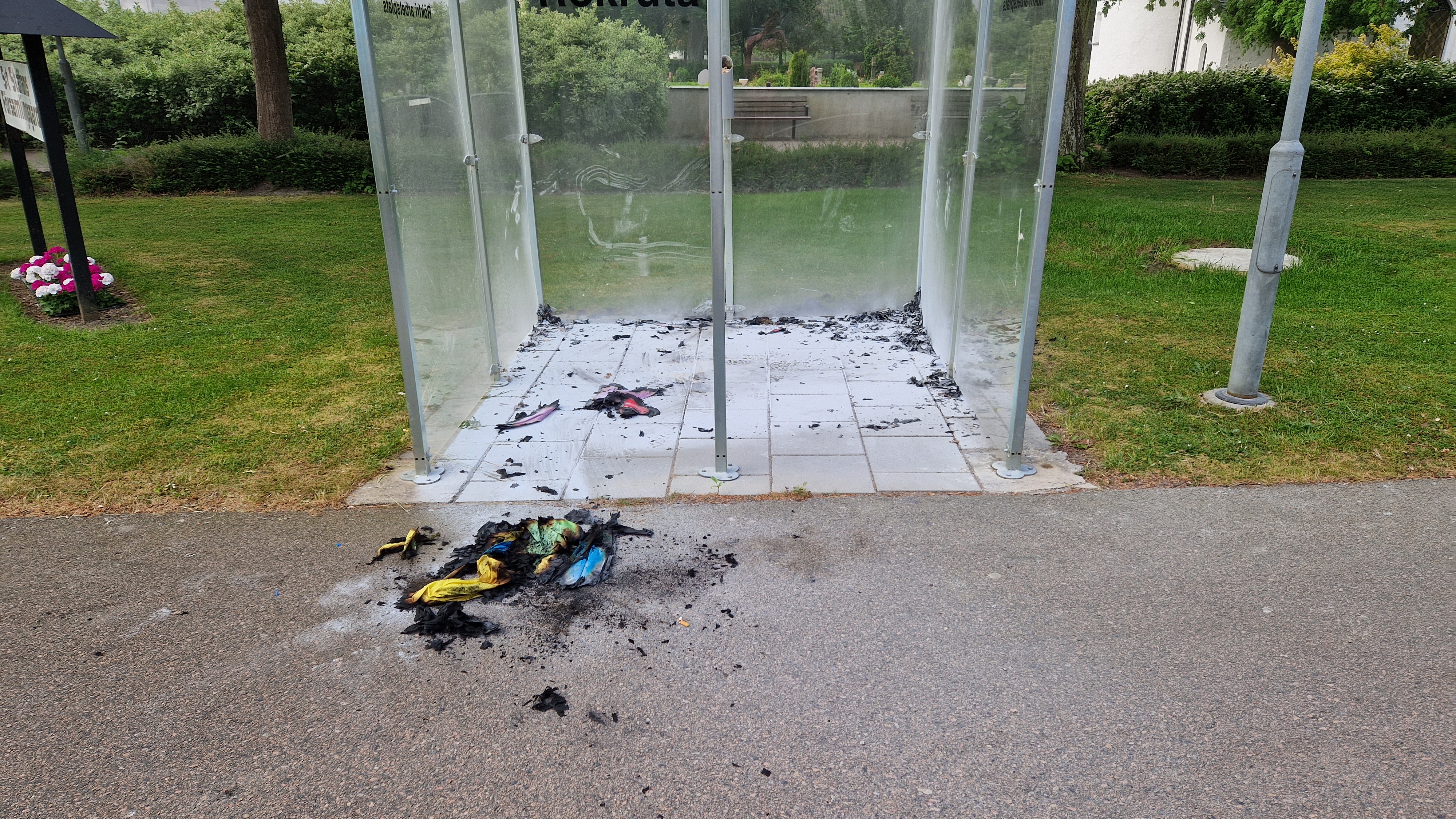 Brända tygbitar av olika färg på marken i och framför rökrutan.