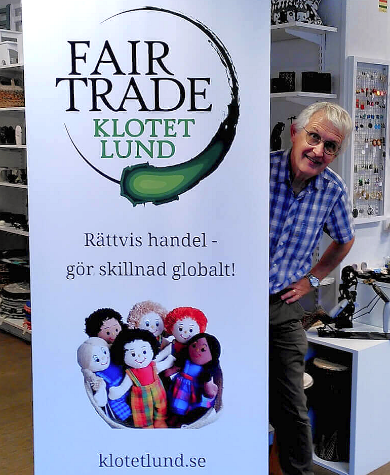 Leende gråhårig man kikar fram bakom en rollup om Fair trade.