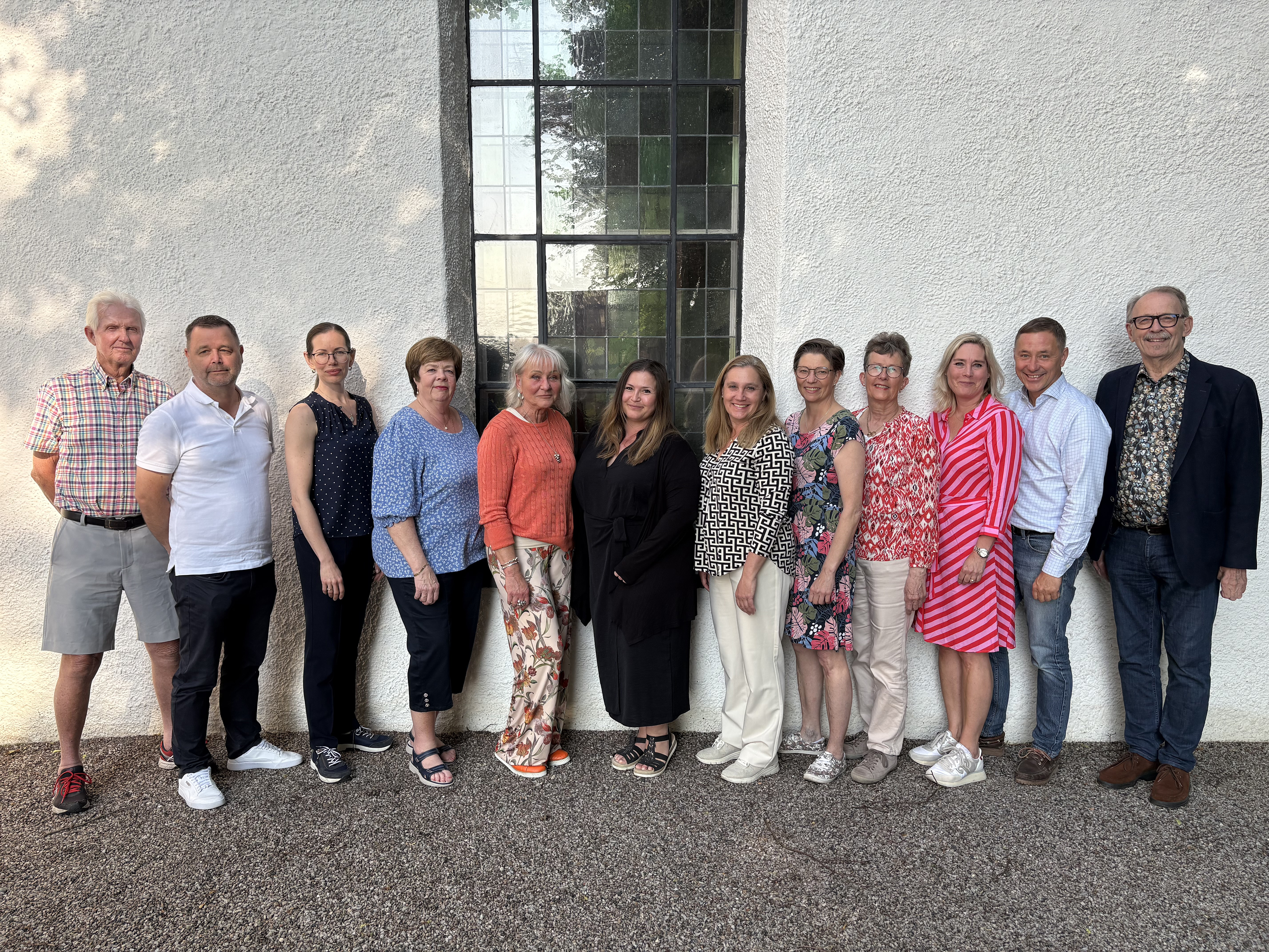 Tolv leende personer framför en kyrkovägg.