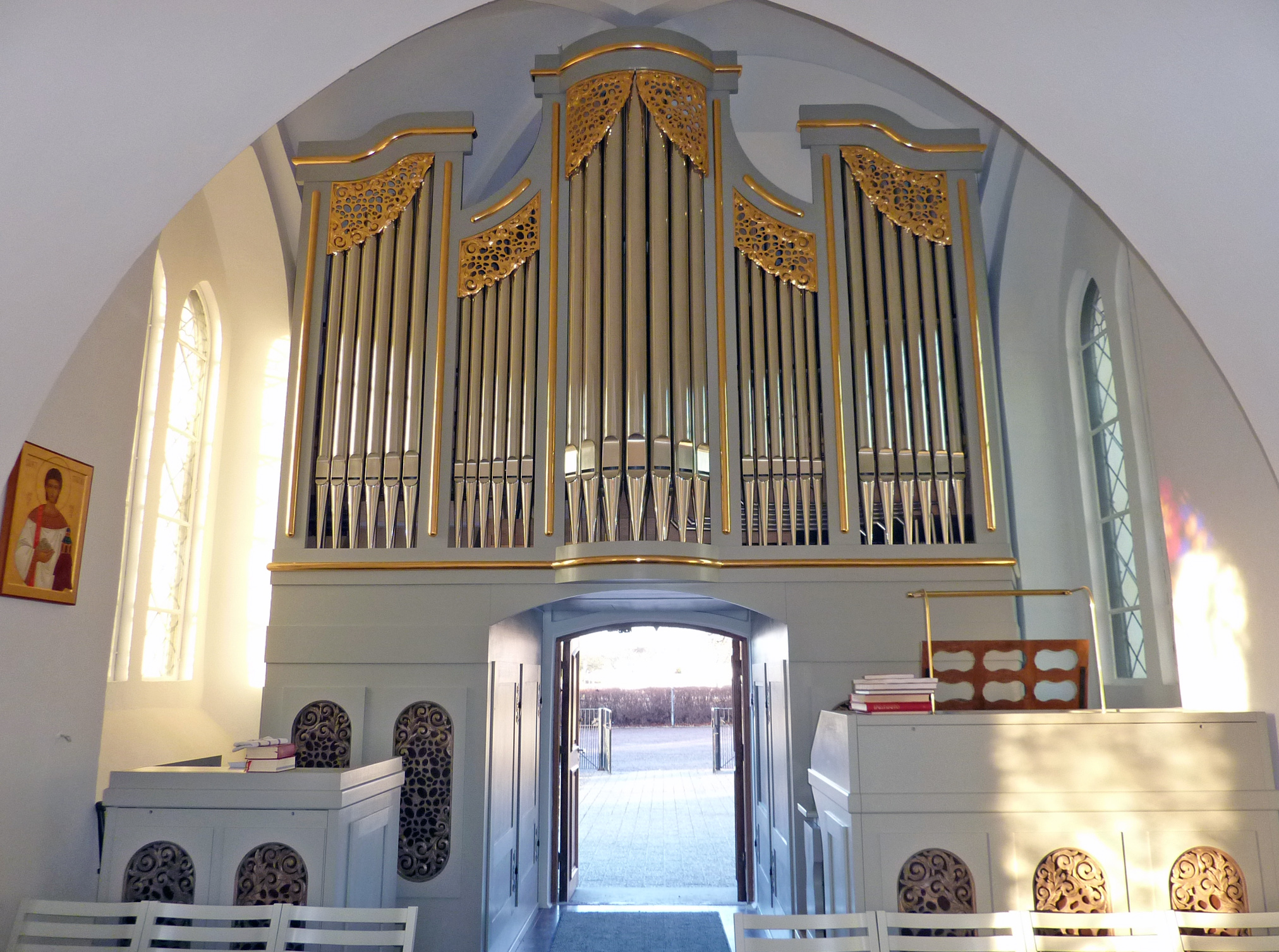 Orgelfasaden inifrån den solupplysta kyrkan med kyrkoporten öppen.