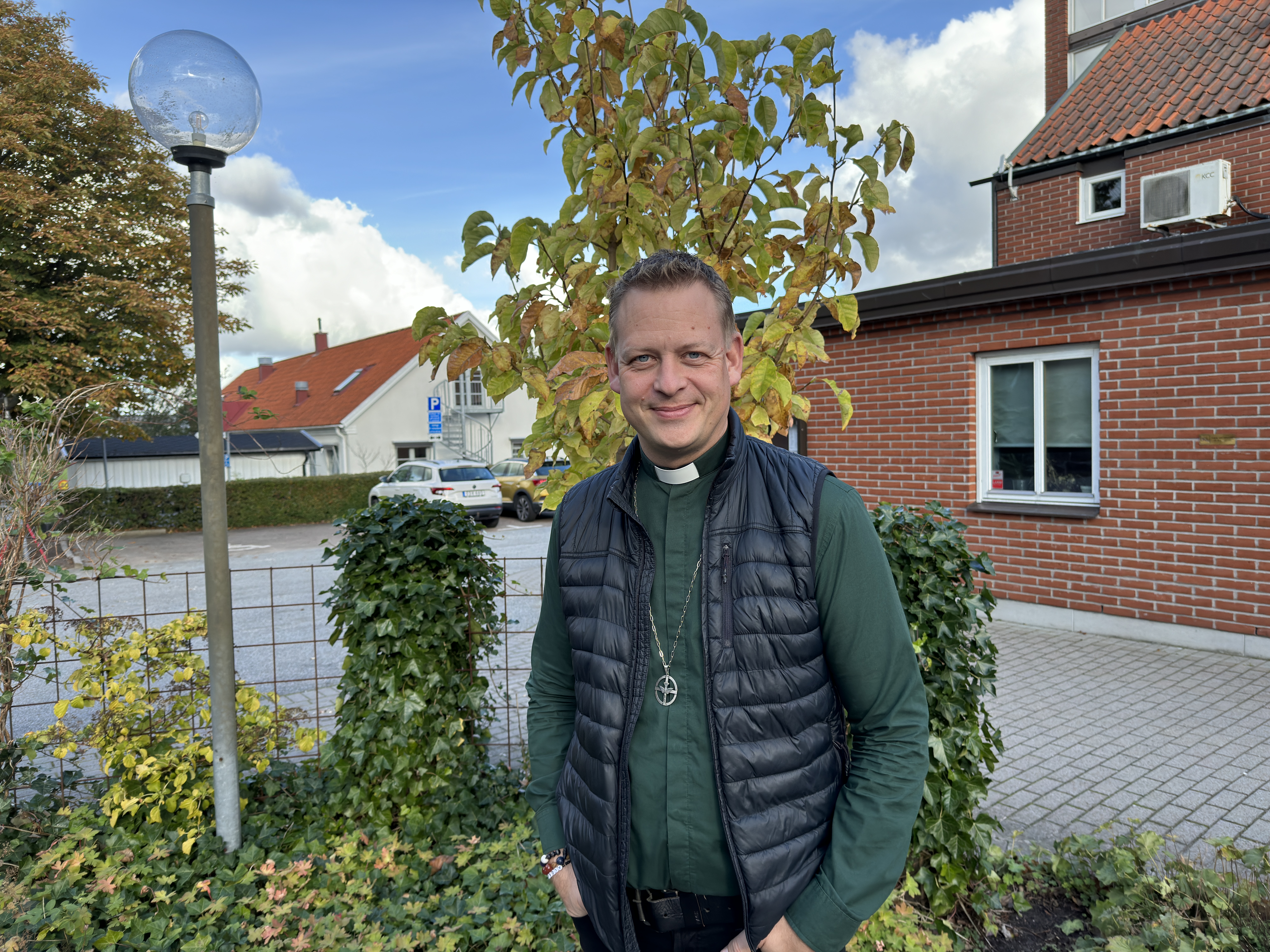 Stefan Kamensky i grön diakonskjorta och diakonemblem framför ett rött tegelhus.