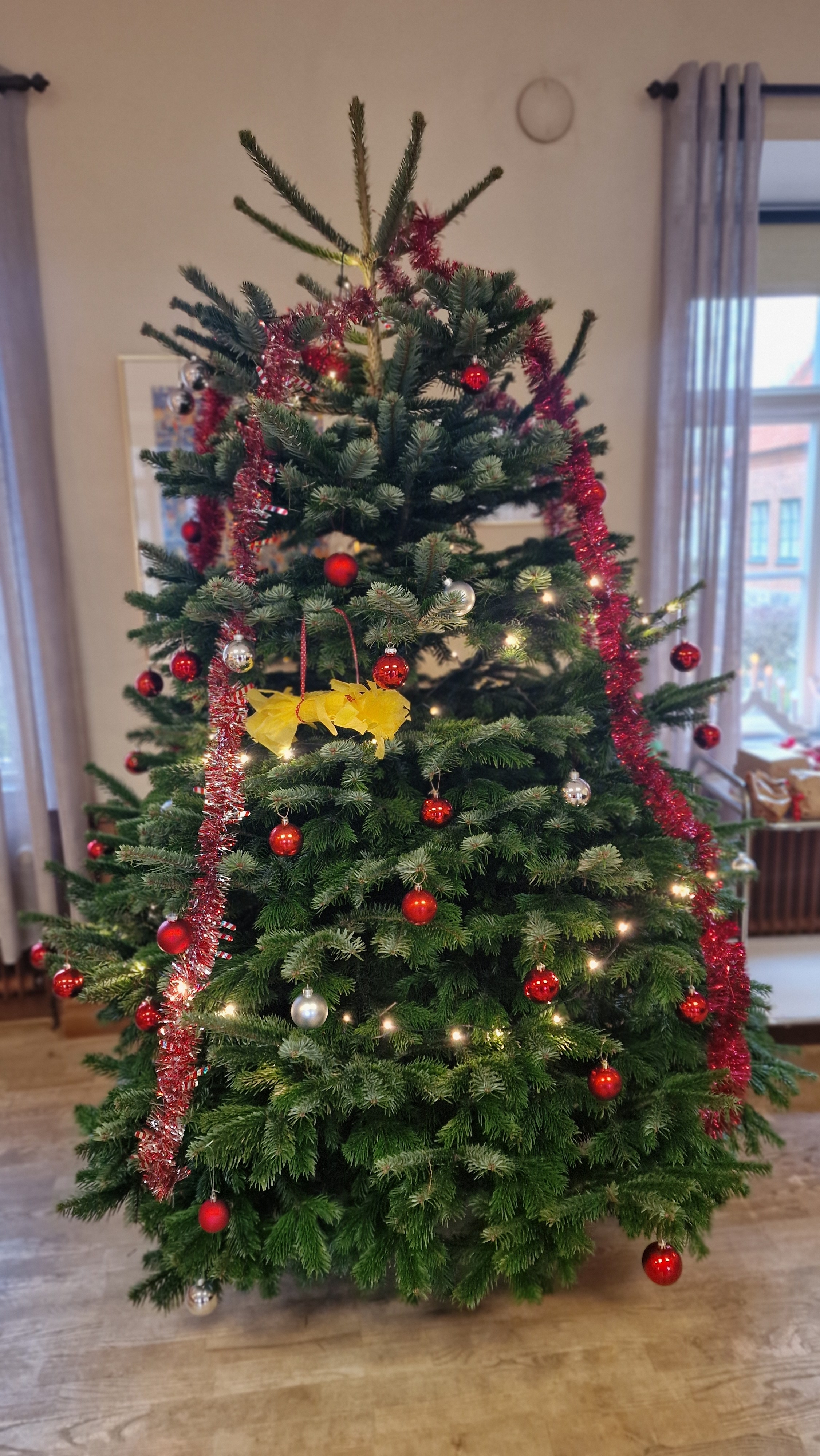 Julgran med rött glitter, ljus och en röd julgranskula.  