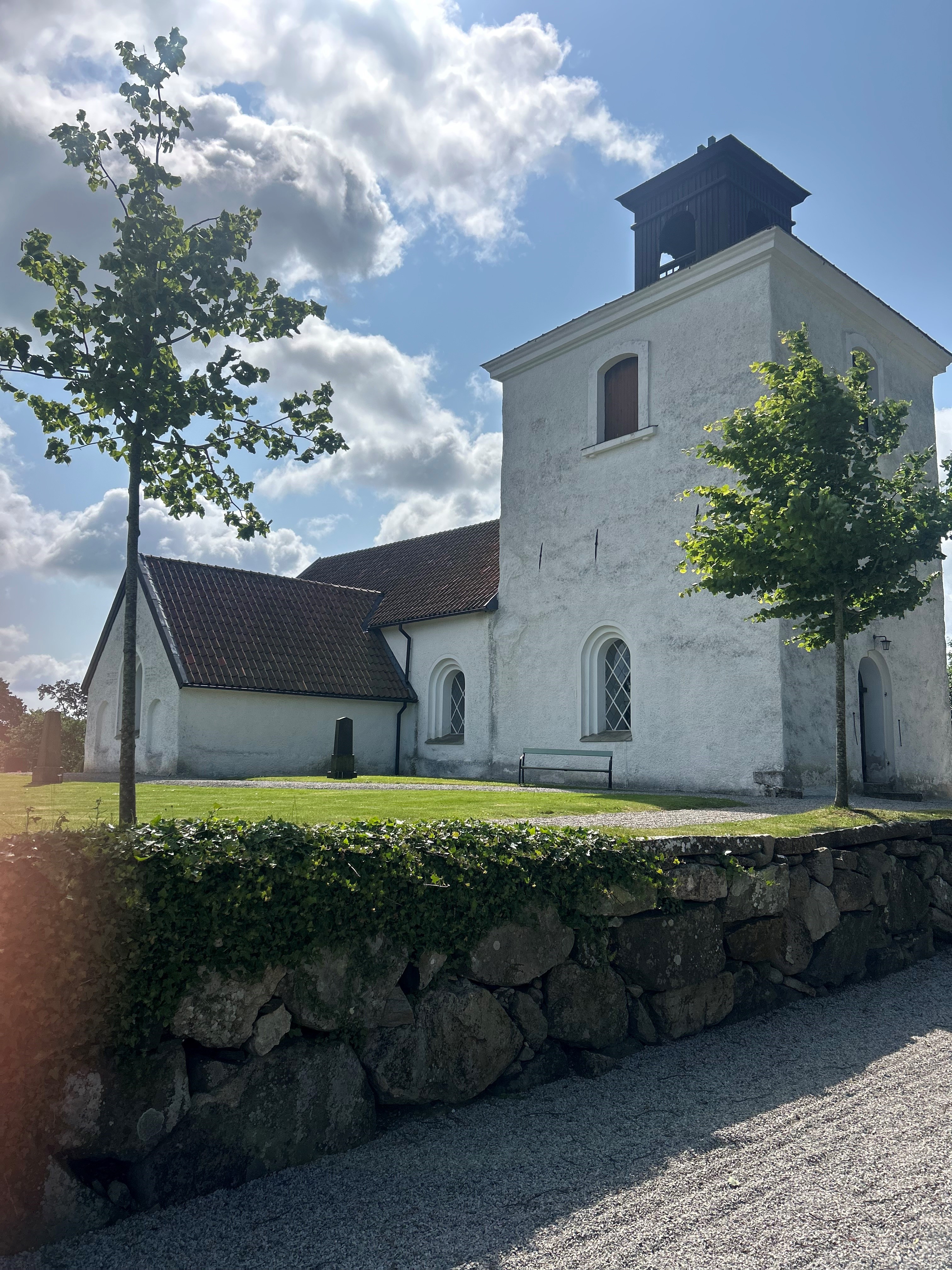 vit kyrkbyggnad med svart tak, med buskage framför.