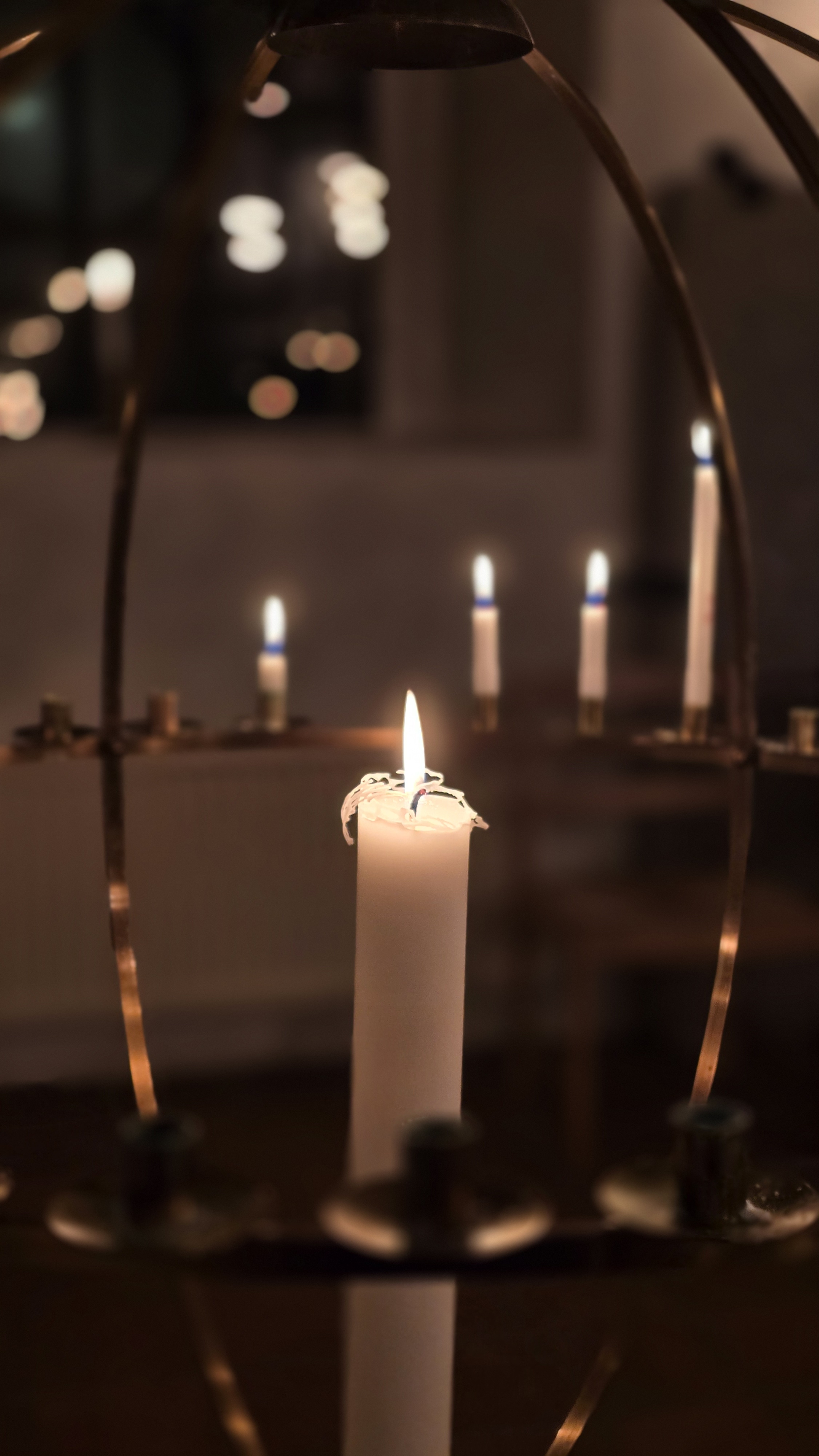 Ljusbärare med tända ljus i en mörk kyrka med vita väggar. 