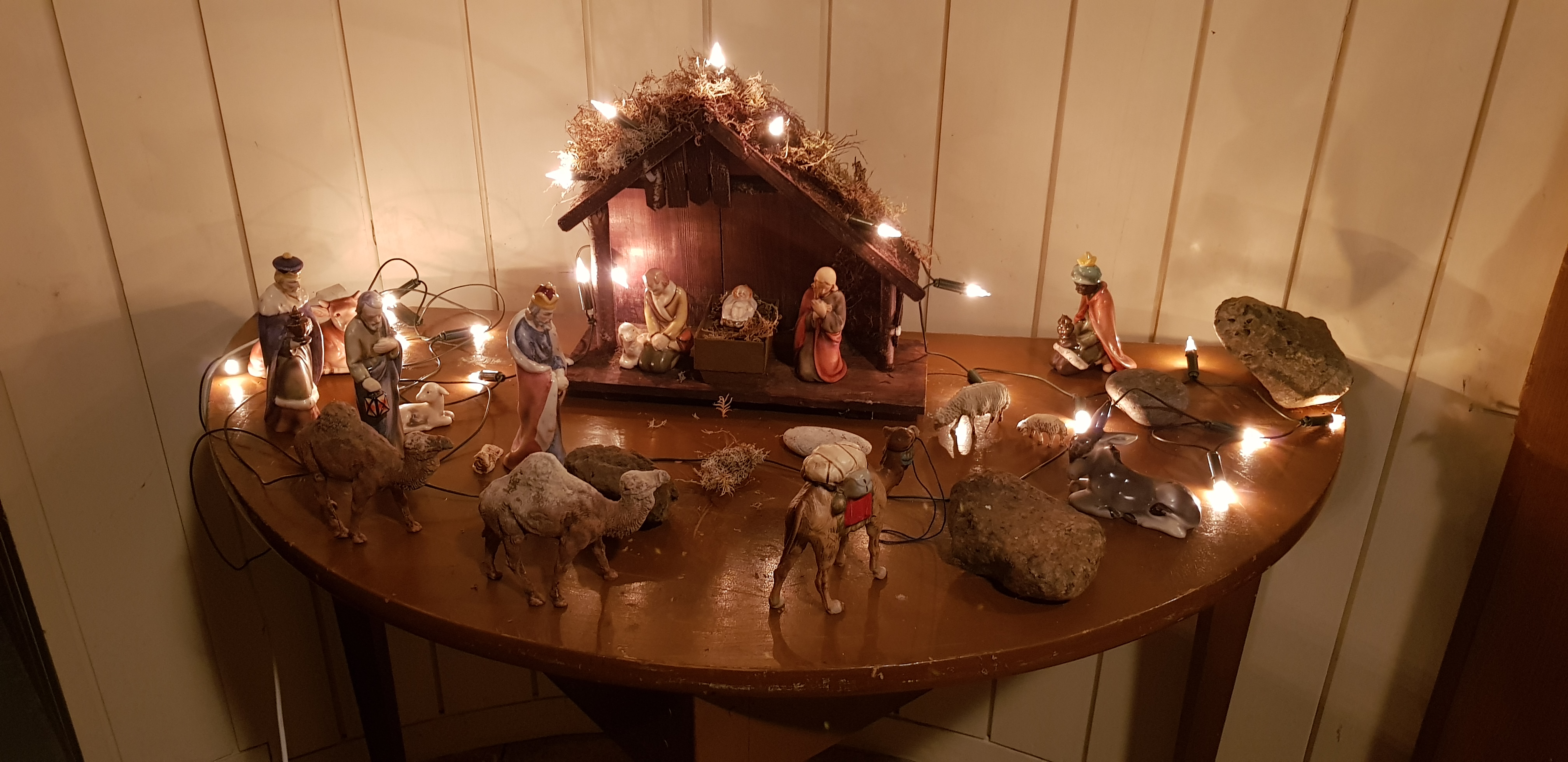 Ett bord med en julkrubba i dunkel belysning, upplyst av en ljusslinga med varm vitt ljus. 