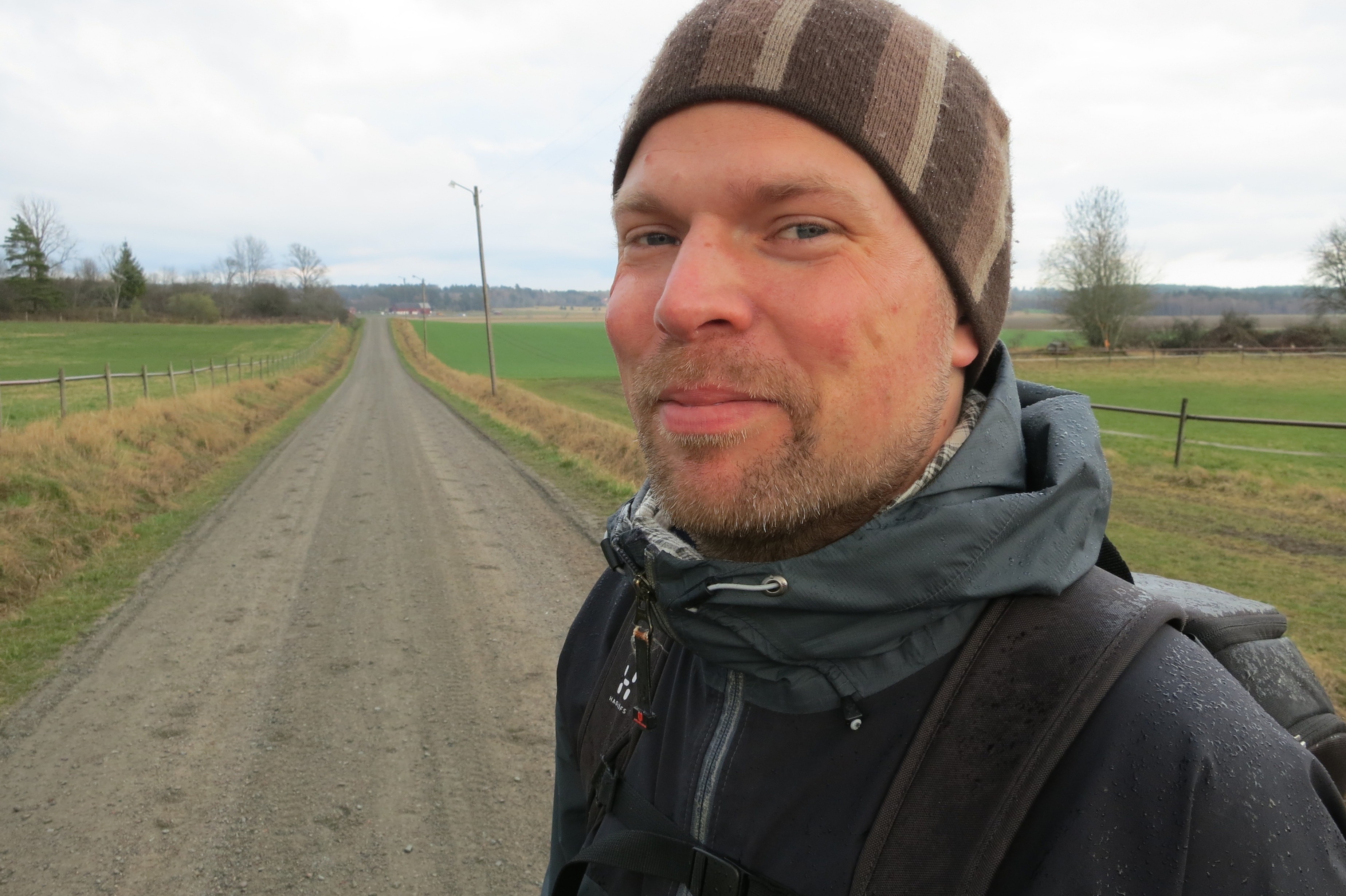 En man med mössa och ryggsäck står vid en väg.