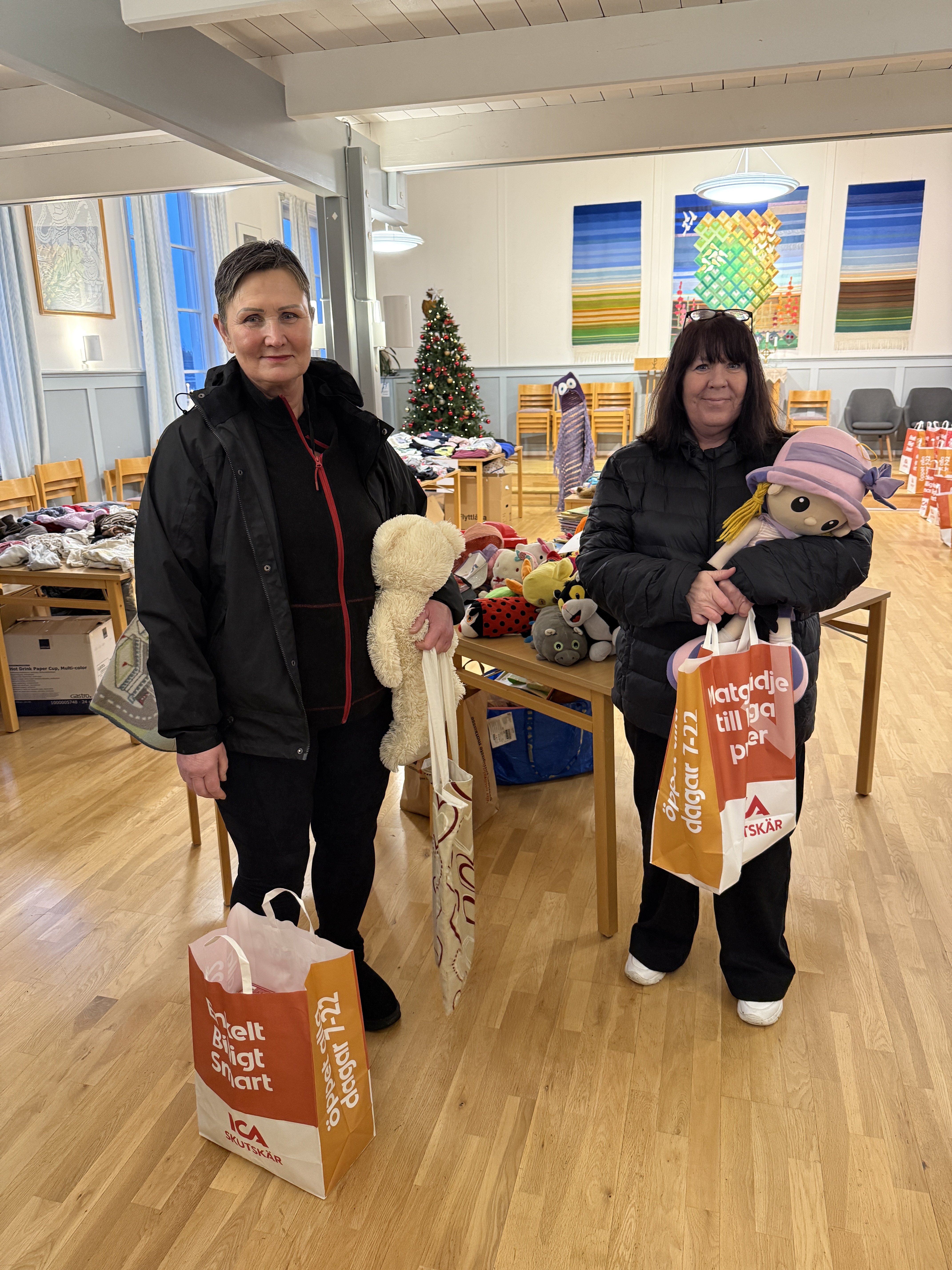Två stående kvinnor håller i varsin papperskasse och mjukisdjur.