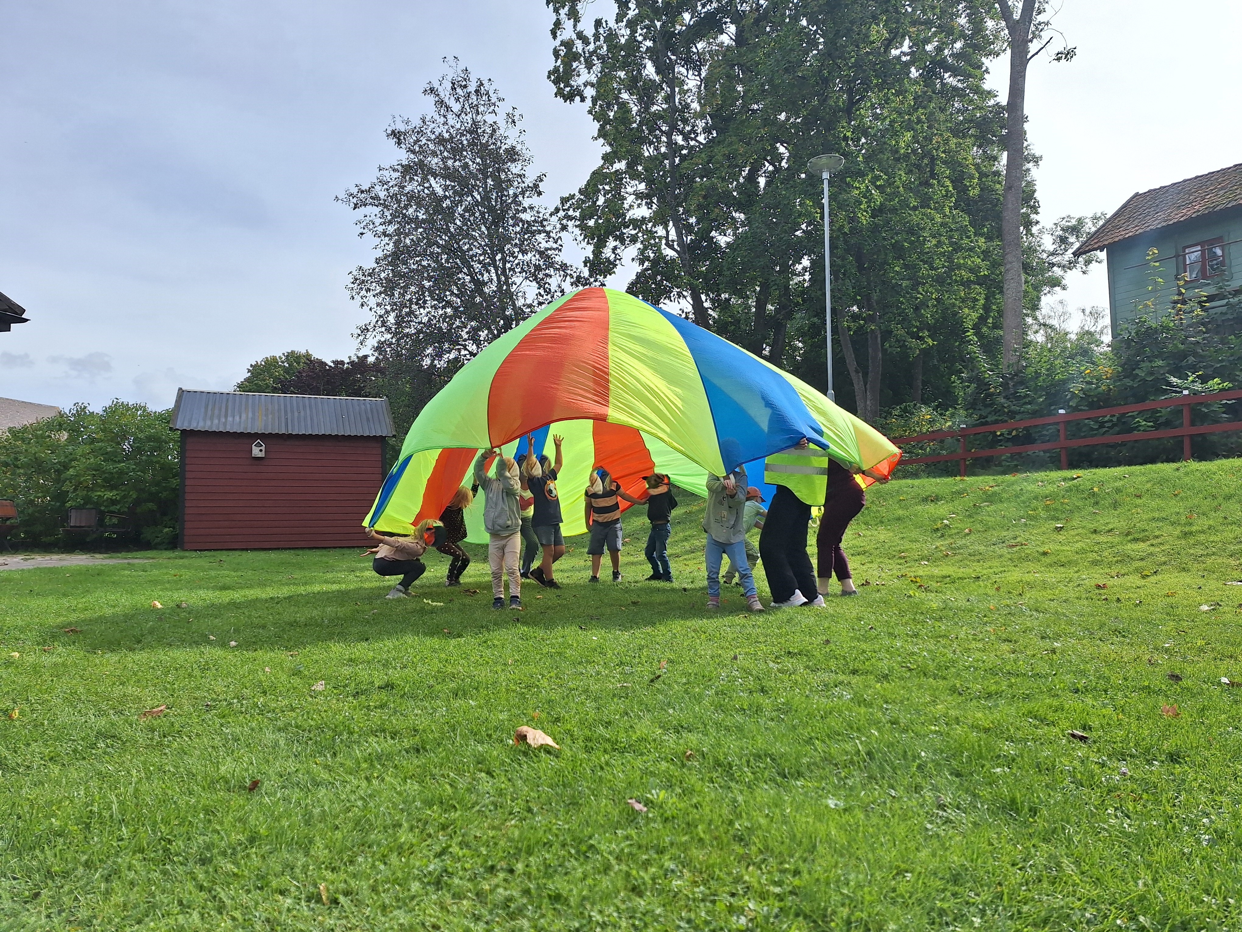 barn och ledare som leker under färgglad fallskärm