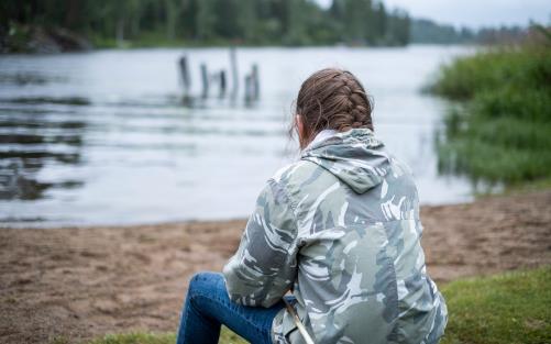 Flicka sitter bortvänd från kameran och ser ut över sjö.