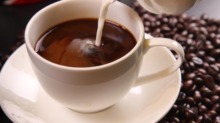En kopp svart kaffe som det hälls mjölk i.