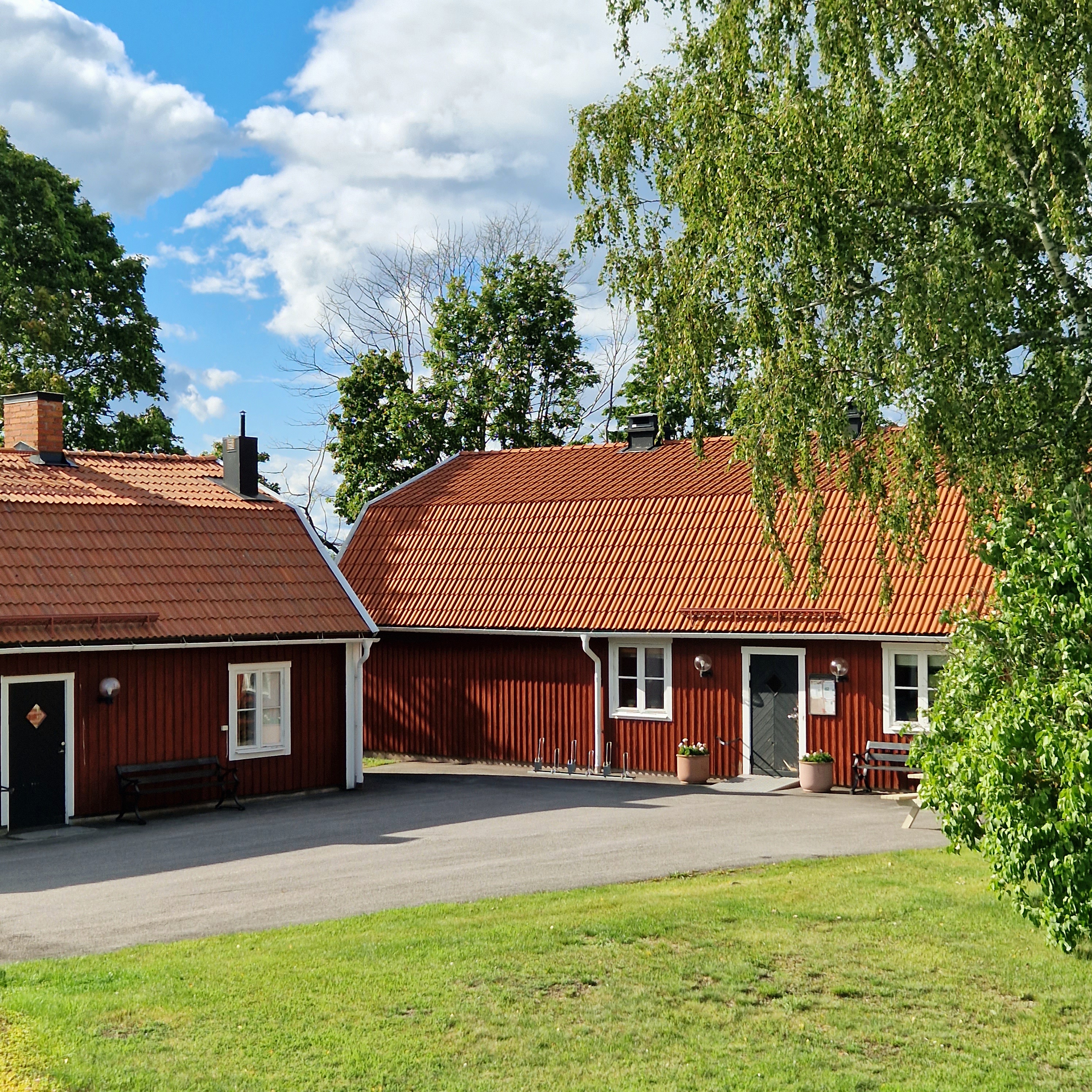 Två faluröda byggnader med vita knutar. i sommartid.