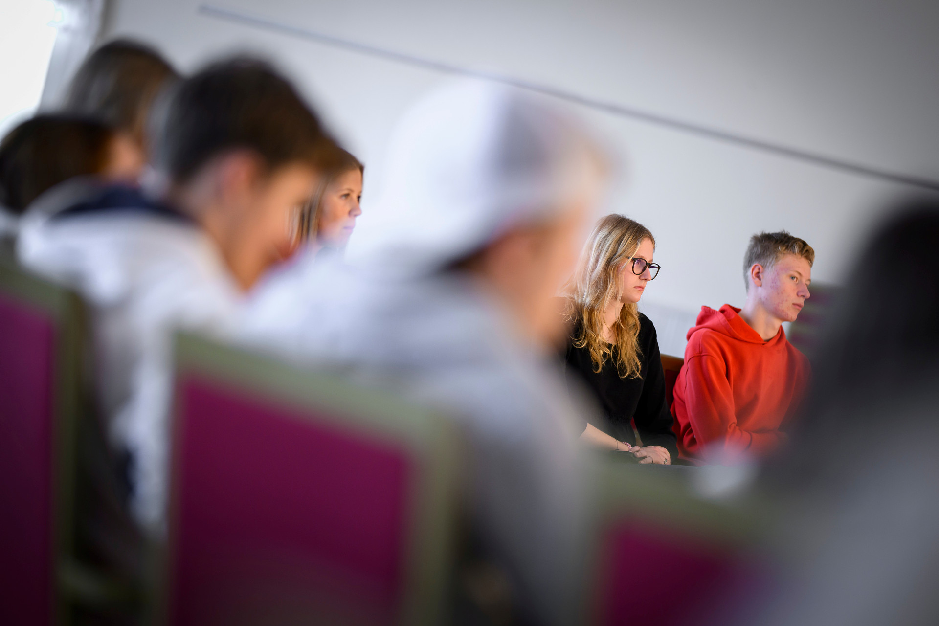 Man ser unga människor som sitter runt ett stort bord. Två ungdomar - en flicka och en pojke syns skarpt medan de andra är suddiga. Man kan tänka sig att det är en undervisningsgrupp eller at de har årsmöte i kyrkans ungdom. 