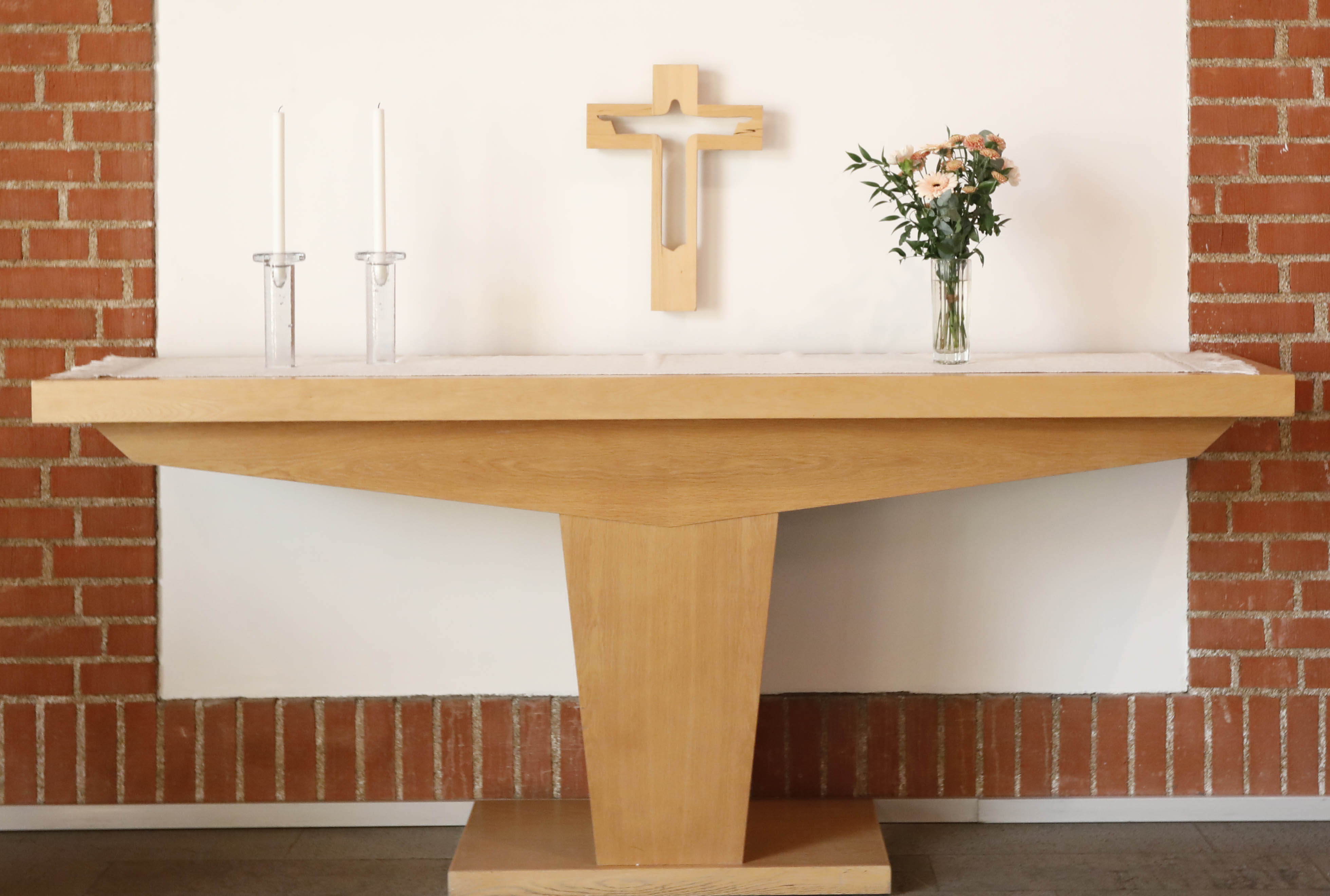 Altare av ljust trä framför vit vägg med tegel runt om.