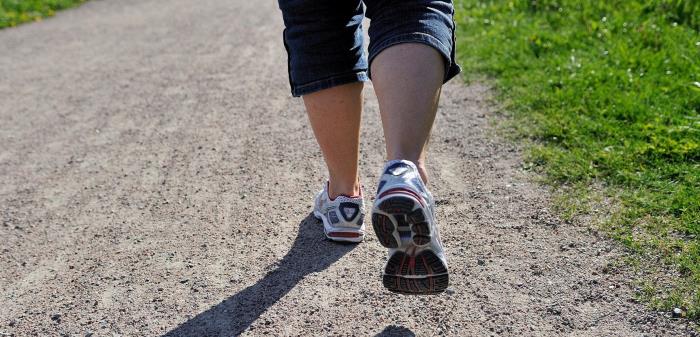 Ben med korta jeans och gympaskor på promenad på grusväg kantad av grönt gräs.