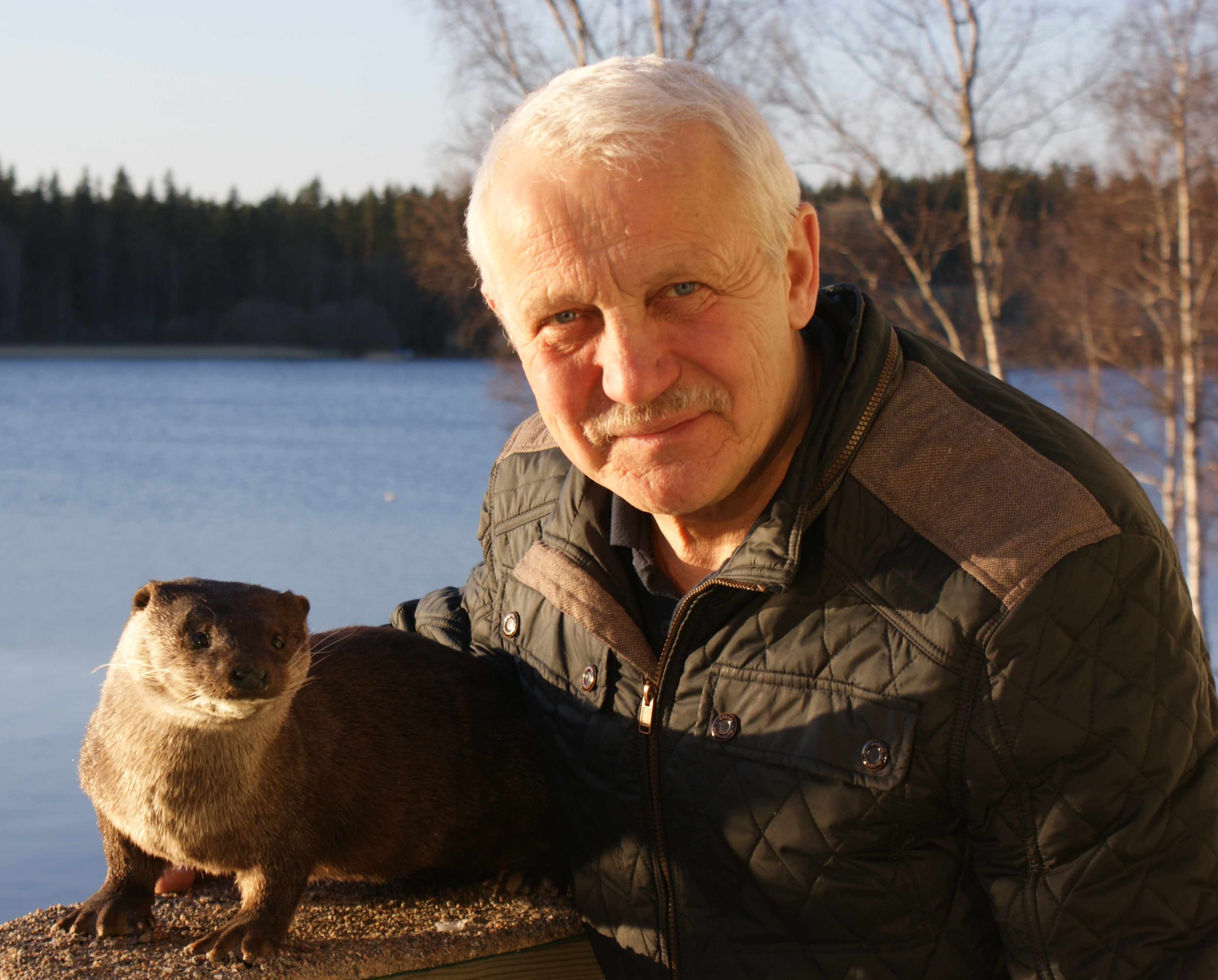 Man med vitt hår vid en sjö med en utter framför sig.