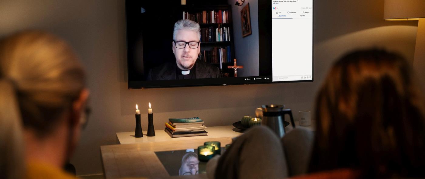 Två personer sitter i en soffa och ser på TV-gudstjänst.