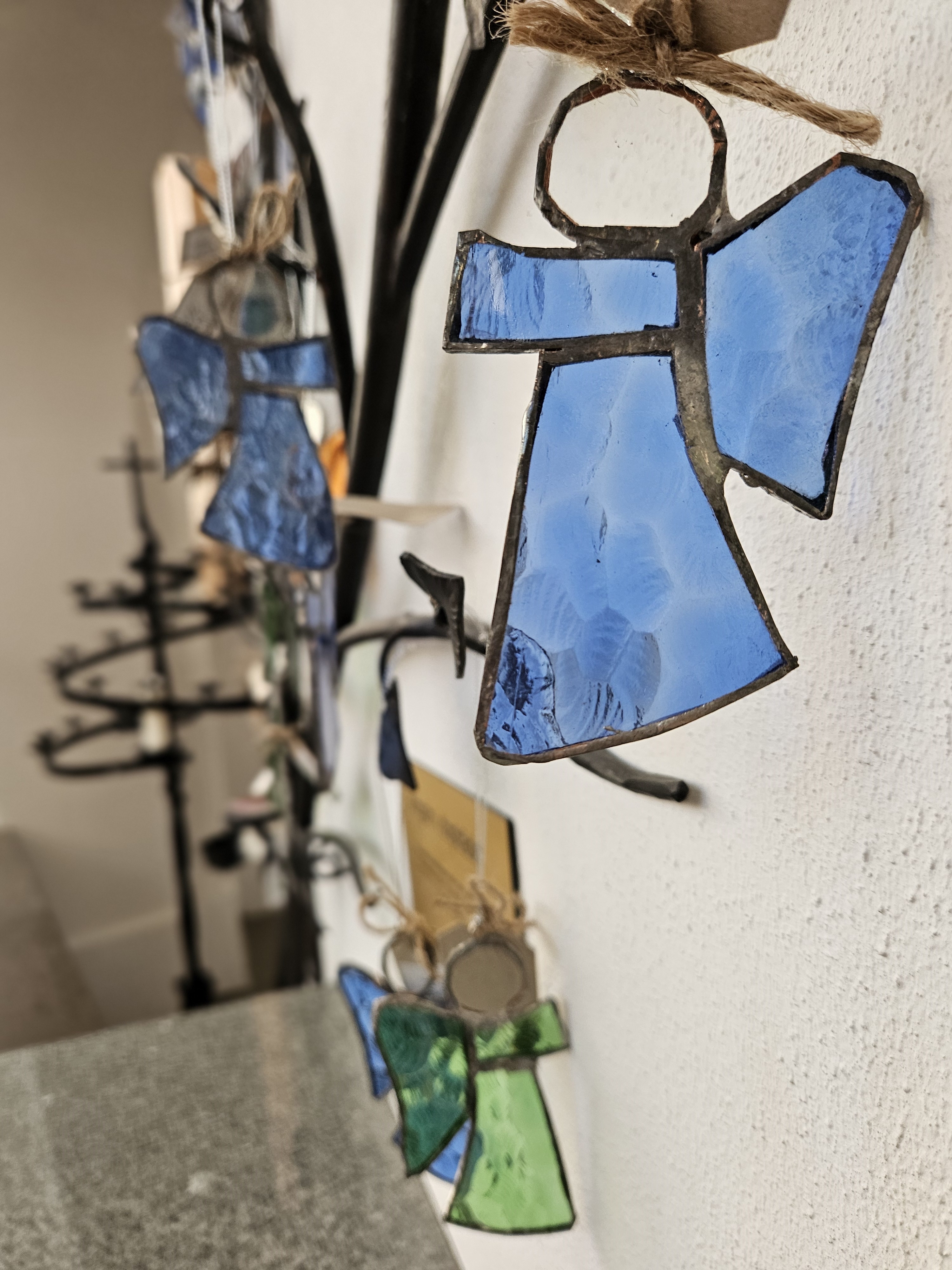 Glasänglar i klara färger hänger från grenar i ett träd av smidesjärn.