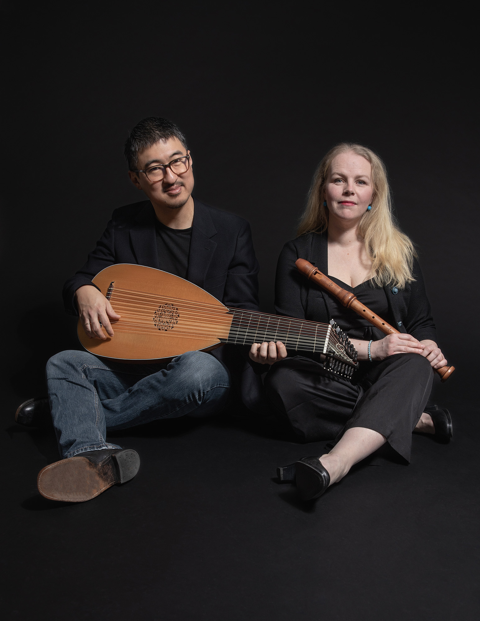 En man i mörk tröja och blå jeans spelar luta. En kvinna med långt ljust hår sitter bredvid.