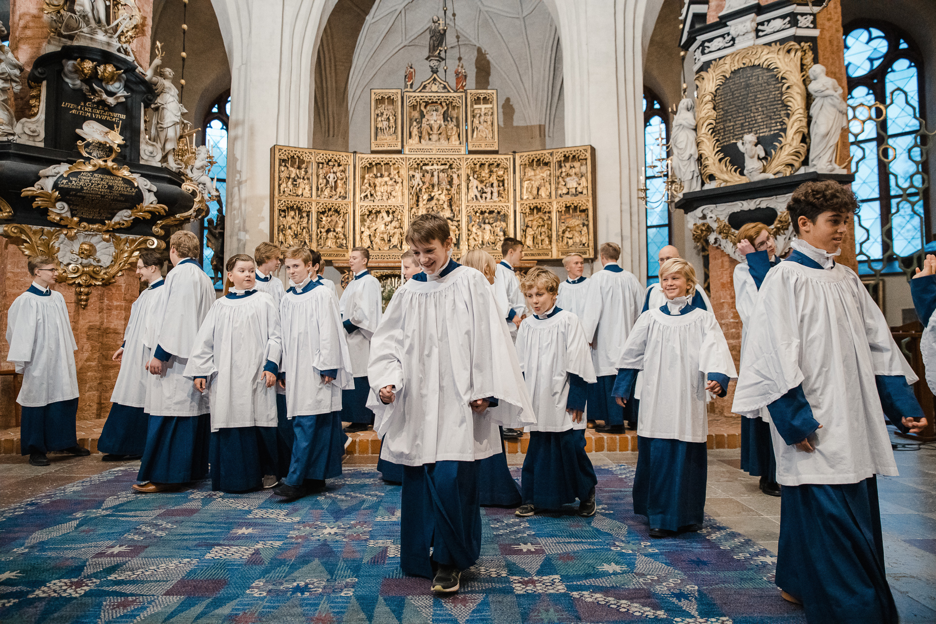 Pojkar i olika åldrar står och går i koret i Västerås komkyrka. Det är klädda i blå och vita körkåpor.