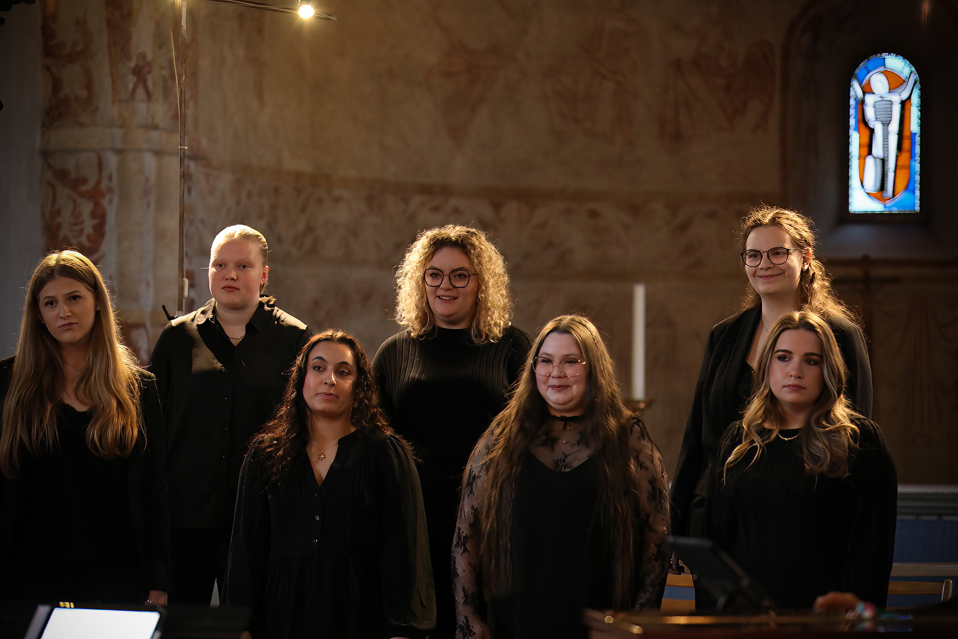 Sju tjejer i svarta kläder står i en kyrka