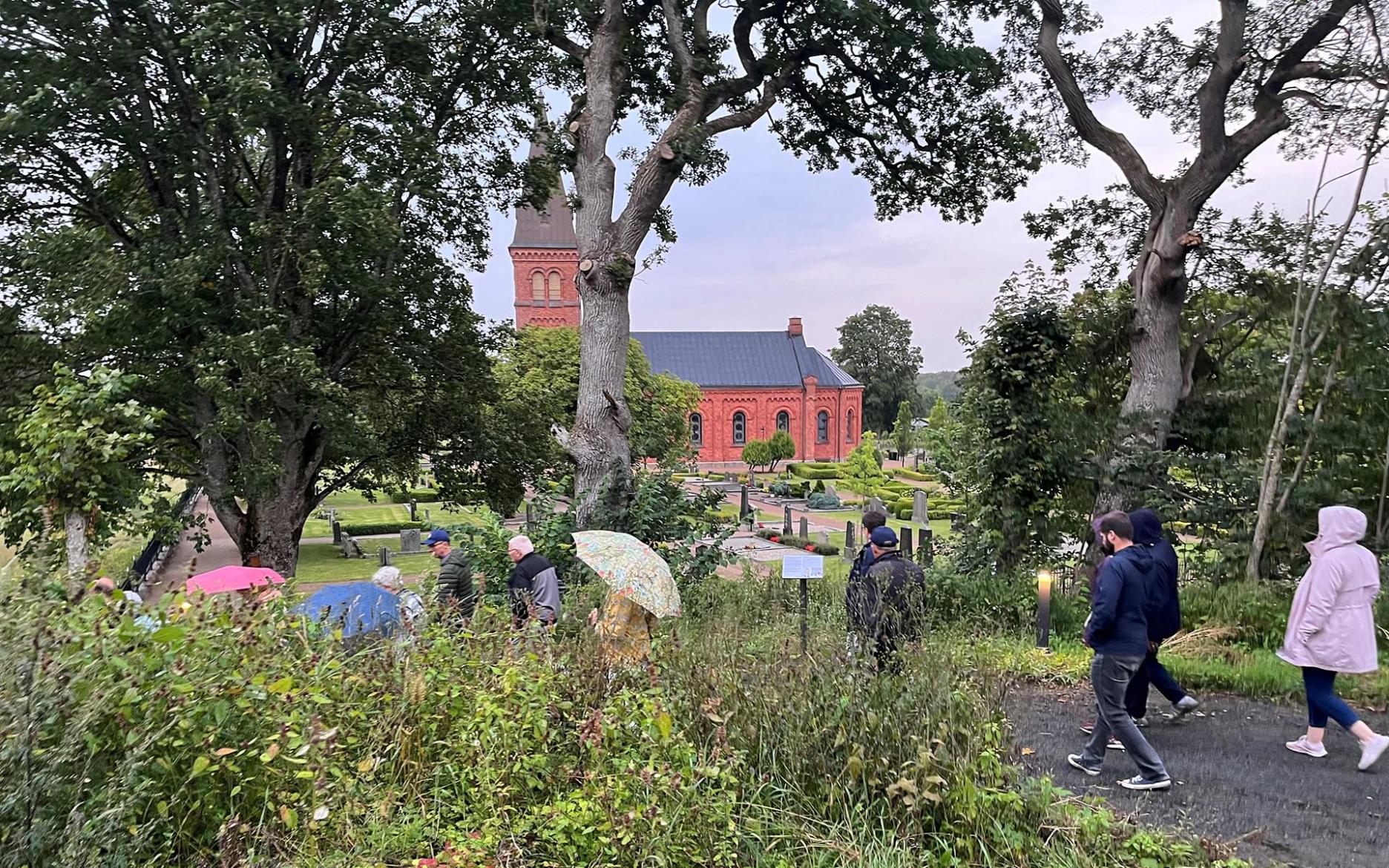Människor på promenad på ny slinga. Ignaberga nya kyrka i rött tegel syns i bakgrunden.