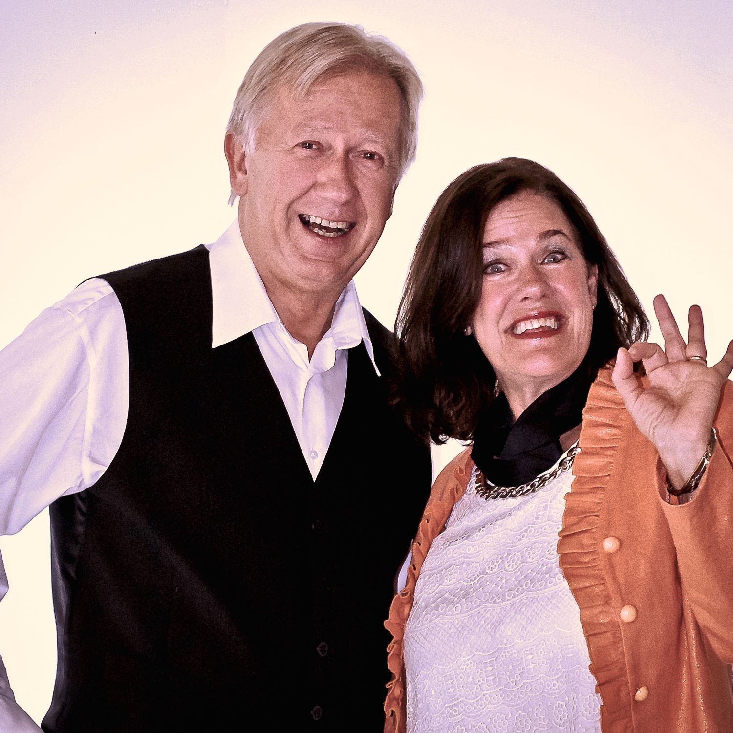 En man i mörk väst och ljus skjorta och en kvinna med mörkt, halvlångt hår skrattar och spexar.