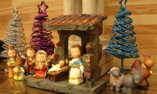 Julkrubba med glada keramikfigurer och tre glittriga granar - en i silver, en röd och en grön.