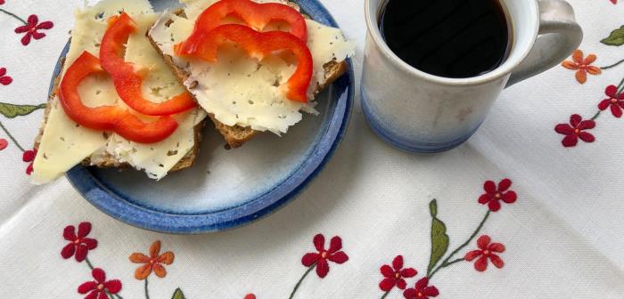 Keramik mugg och tallrik med blå kant, ostsmörgåsar med röd paprika. Kaffe i muggen.