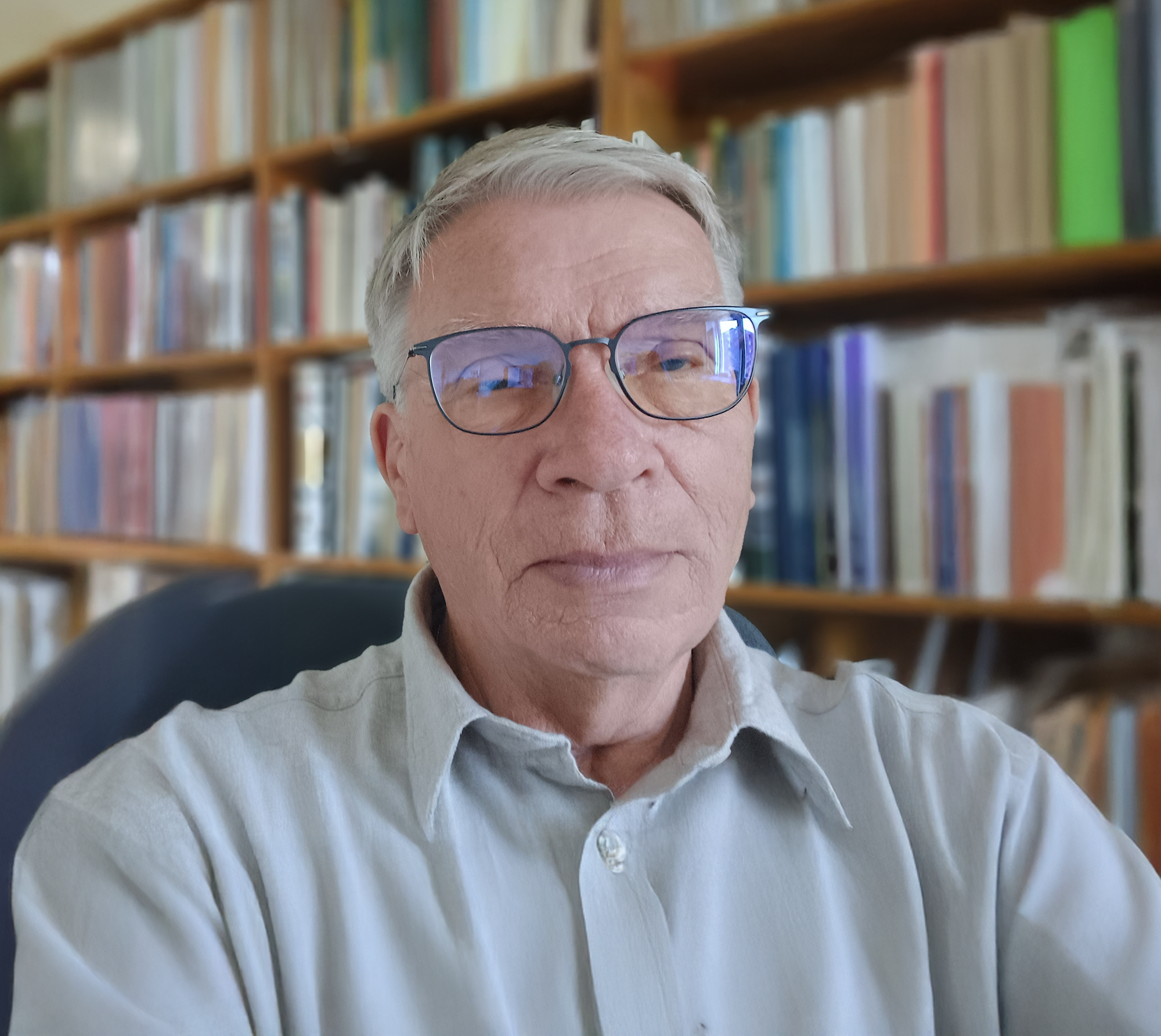 Man med glasögon och ljus skjorta framför välfyllda bokhyllor.