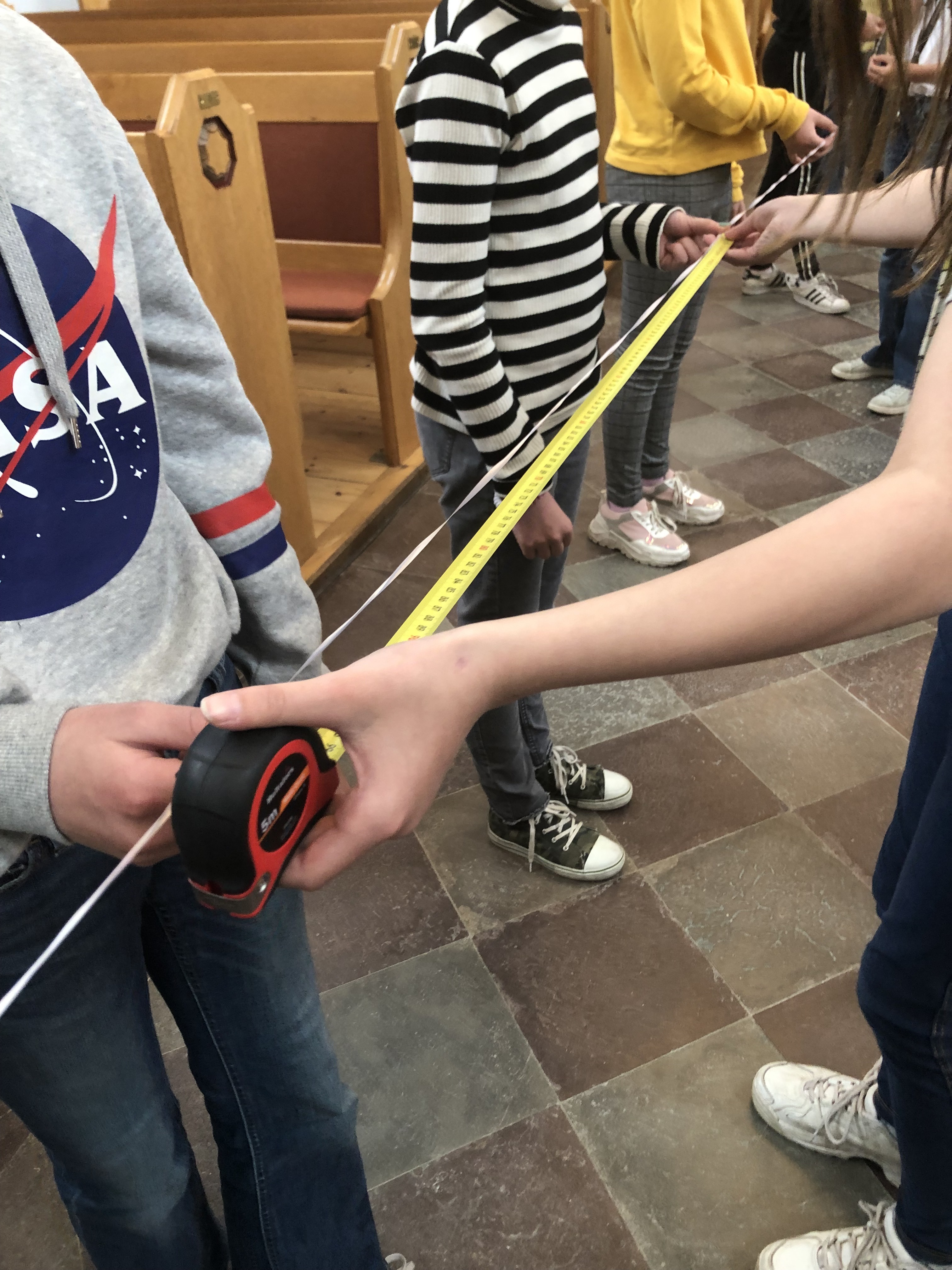 Barn står på rad i kyrkgången och håller i ett måttband för att mäta.