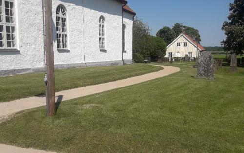 Hårdgjord grusgång svänger sig längs med den vita kyrkan med rött tak. Grön gräsmatta.